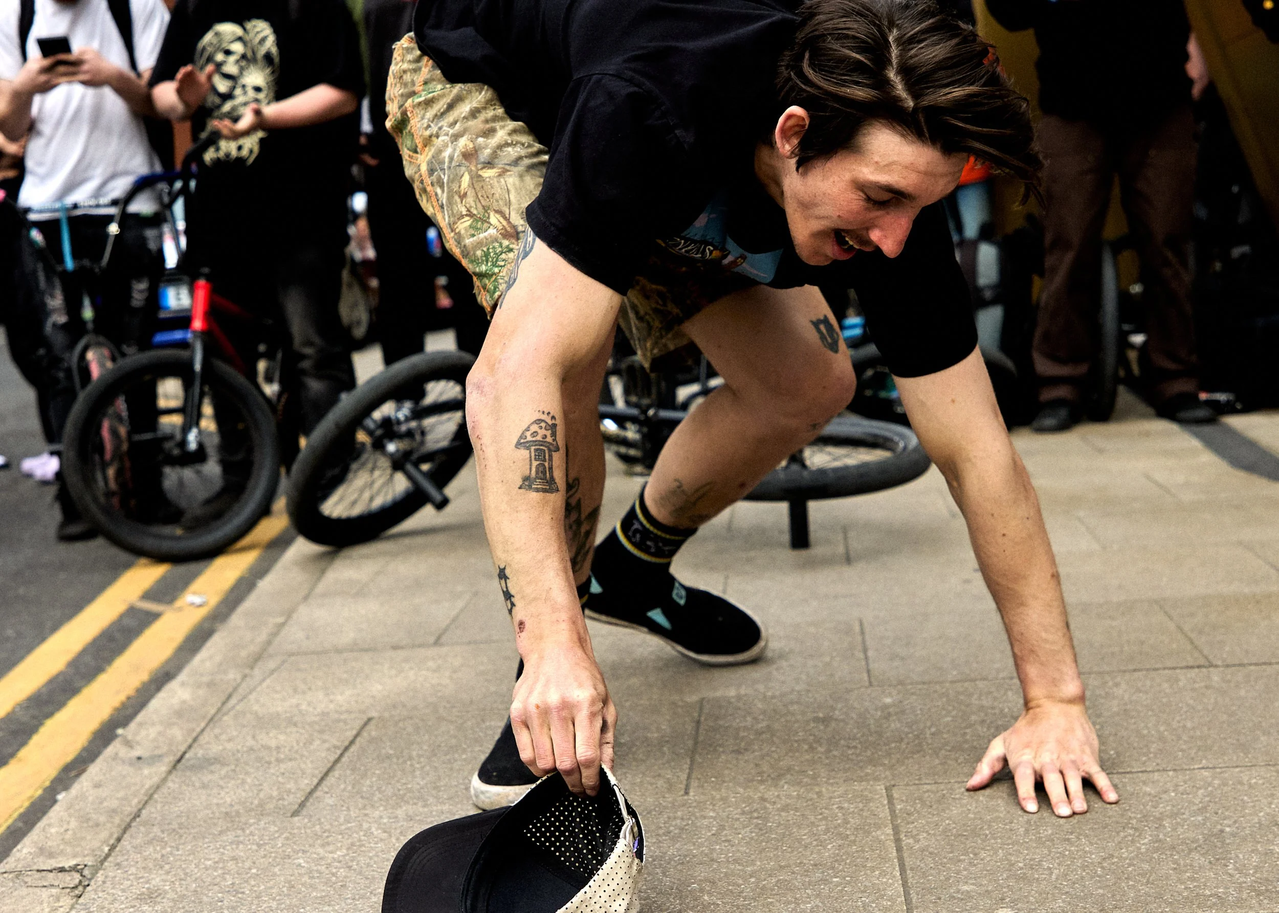 A person with tattoos crawling on the sidewalk, smiling, surrounded by onlookers and bicycles.
