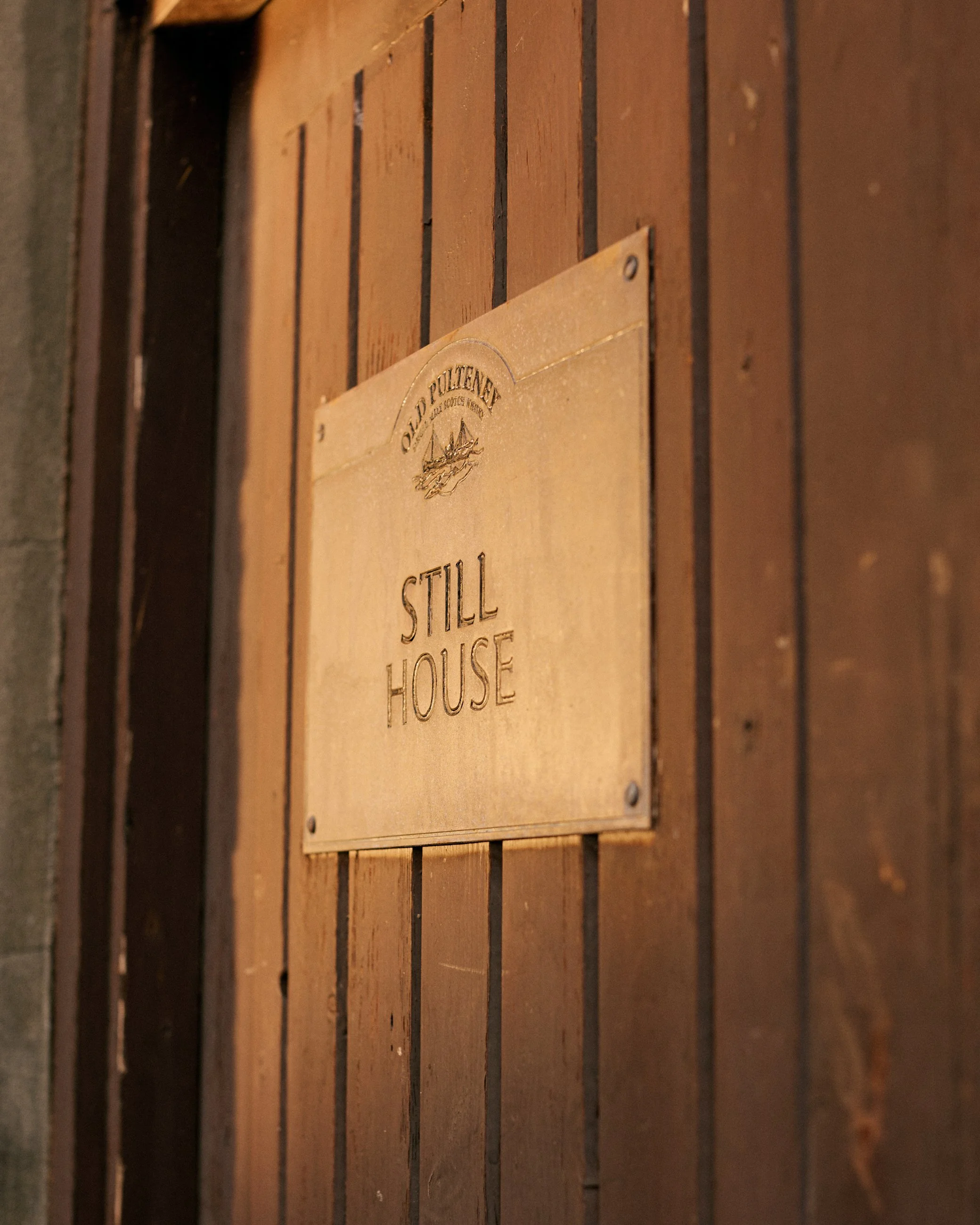 A wooden plaque with engraved text that reads "Old Potlatch Still House," mounted on a wooden wall.