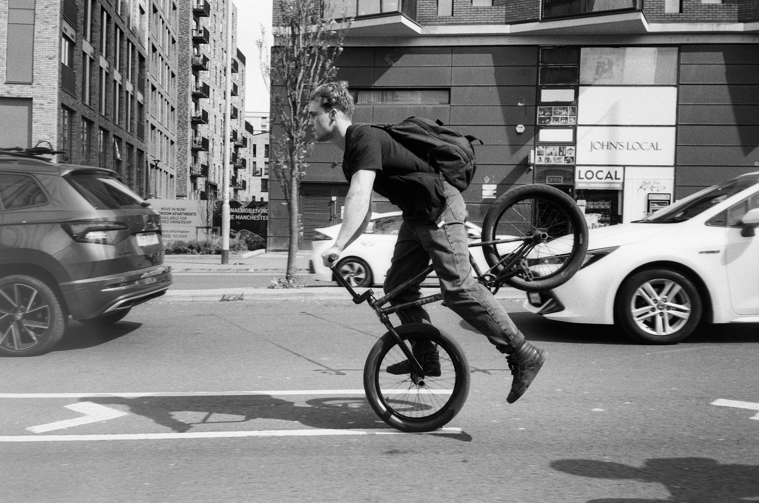 A person performing a bicycle stunt, balancing on the front wheel while riding on a city street with cars in the background.