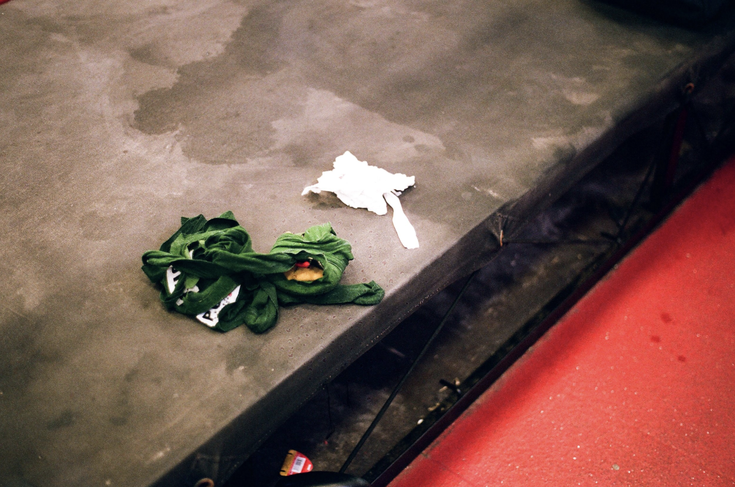 A crumpled white used tissue and a crumpled green cloth or jersey on a gray padded bench with a red floor underneath.
