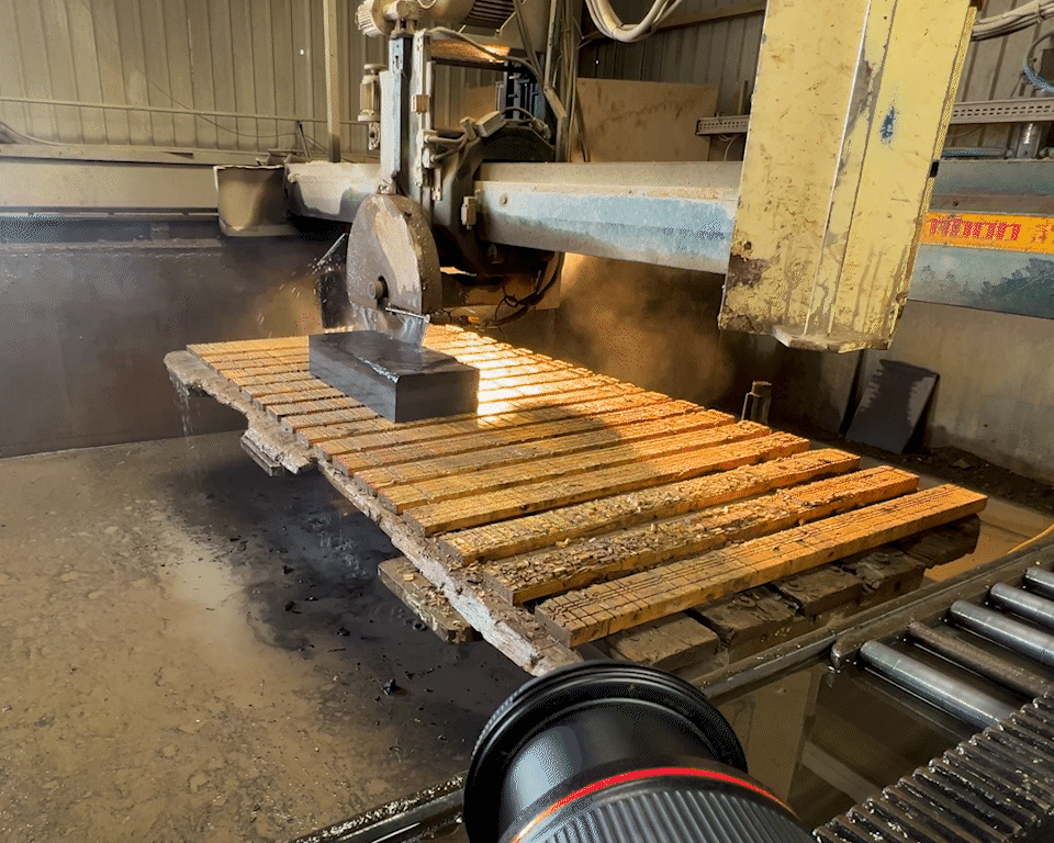 Industrial cutting machine slicing large metal block, with sparks and fire visible, on a metal worktable in a factory or workshop.