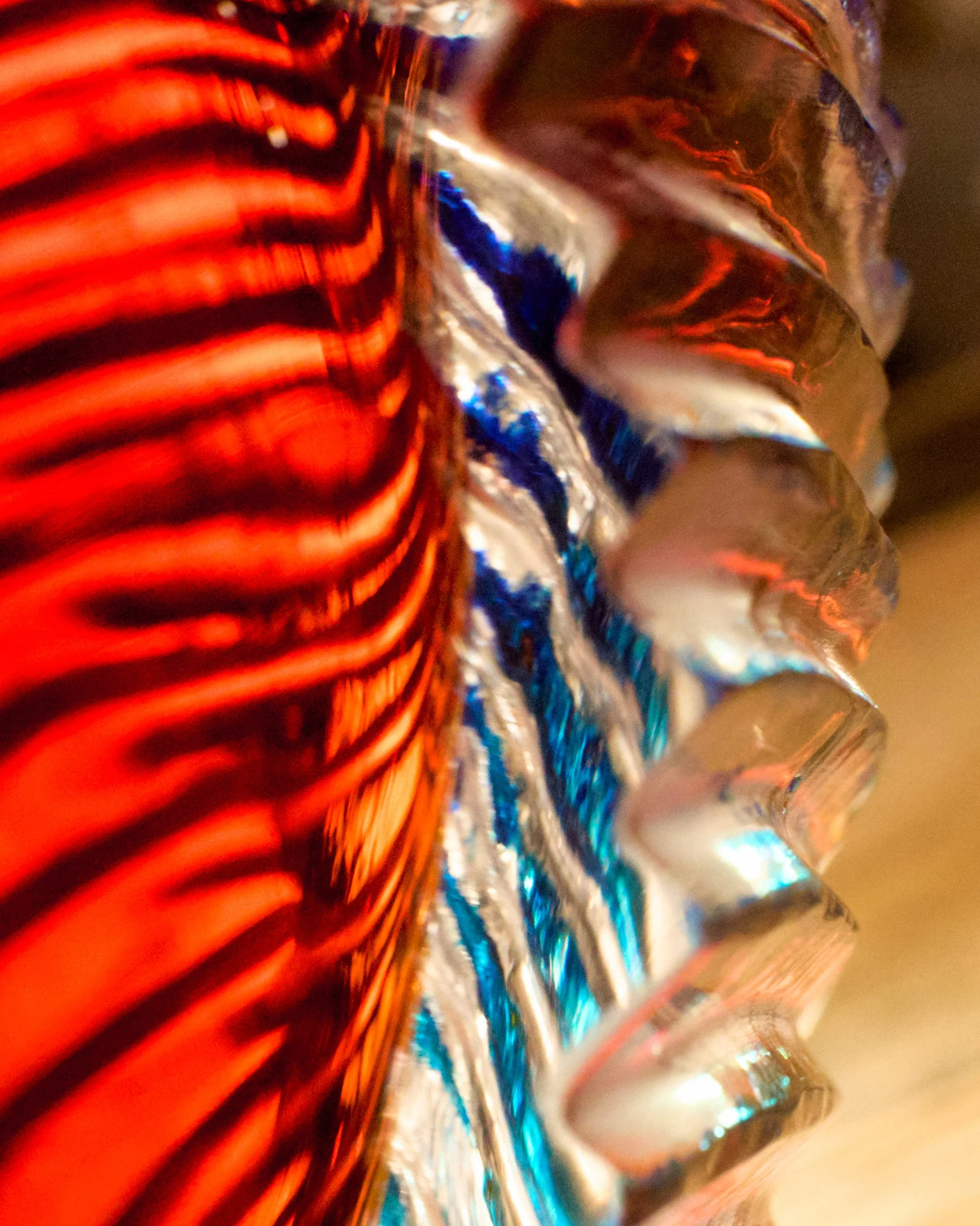 Close-up photo of a metallic and colorful object with red, blue, and silver reflections, featuring a row of corrugated, jagged edges.