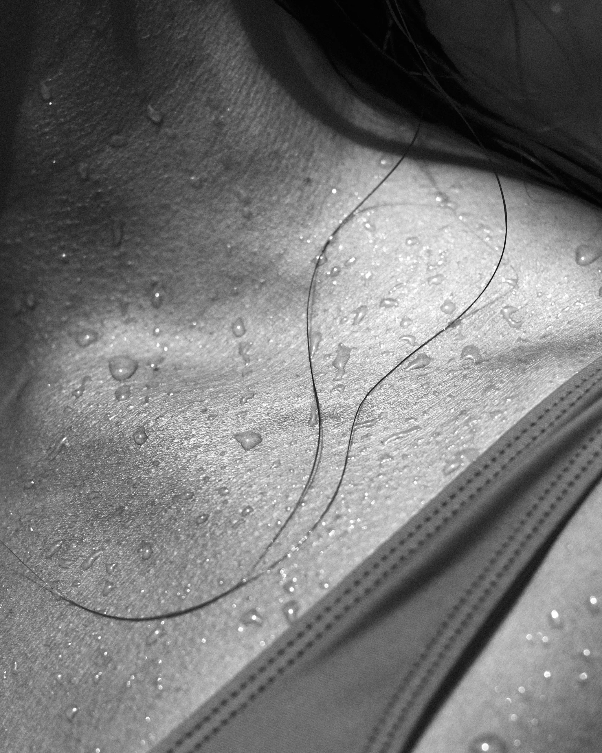 Close-up of a wet, textured surface with scattered water droplets and a thin, curved hair lying on it.