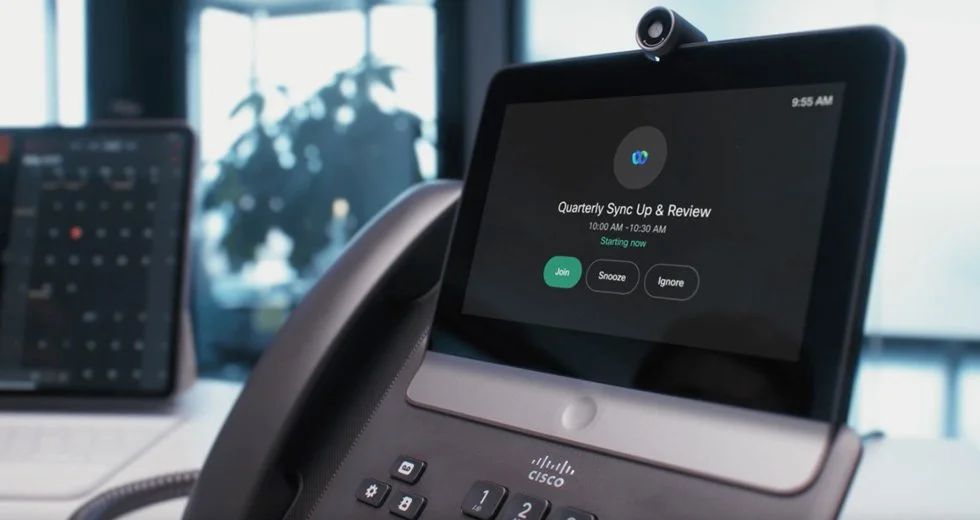 A conference phone with a touchscreen display showing a scheduled online meeting titled "Quarterly Sync Up & Review" with options to 'Join,' 'Snooze,' or 'Ignore.'