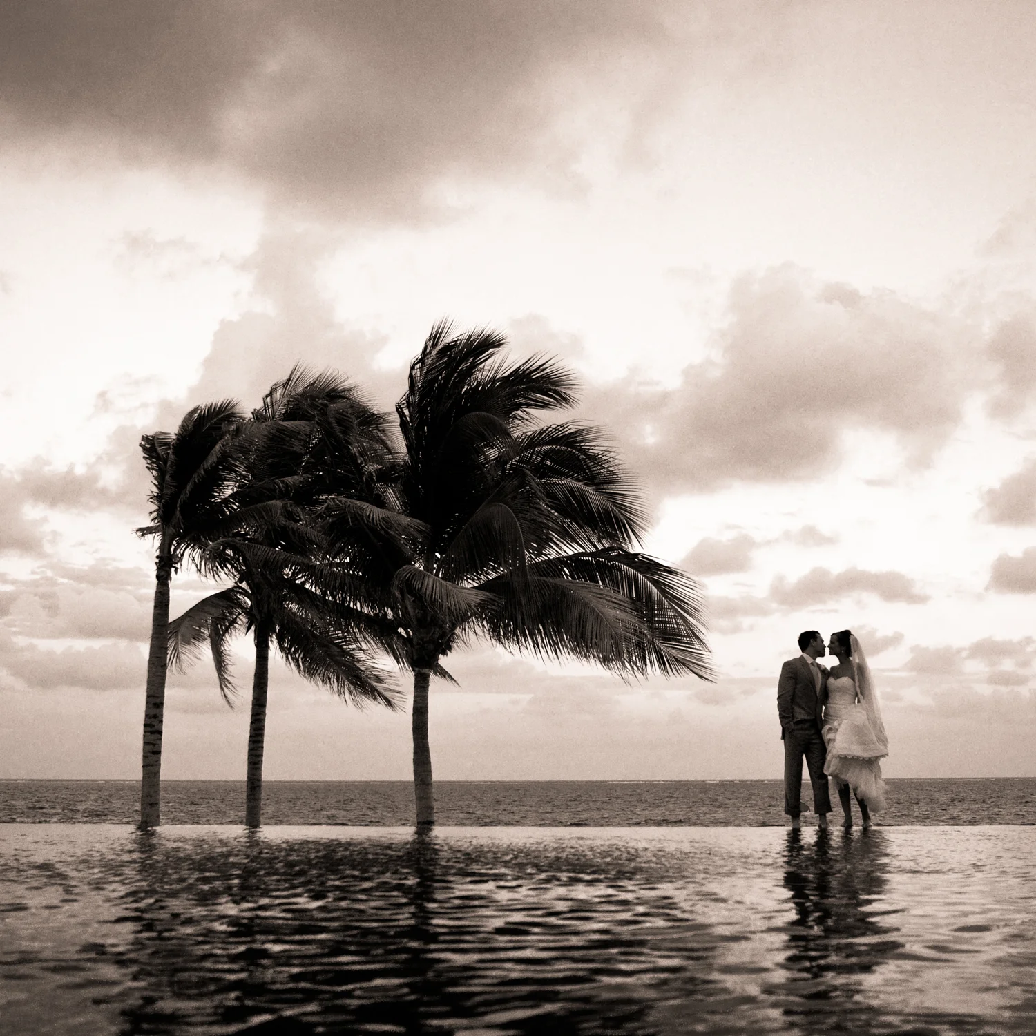 Erin & Robbie - Riviera Maya - This shot is one I had visualized the day before sitting beside the pool. The other side of the wall of the pool is what they're standing on and it's not thick, it was only about a foot or so wide with water flowing over. And there's a drop on the other side and then you see the ocean in the background. So as the sun was really setting on their wedding day, really almost too late, I begged them, they'll tell you, beggggged them to let me take this shot, which meant walking all the way back to this spot and shimmying out onto the wet edge of the pool with me on the other side. We almost didn't do it, but they felt good about it, the shot took 30 seconds, but took 20min to set up. 