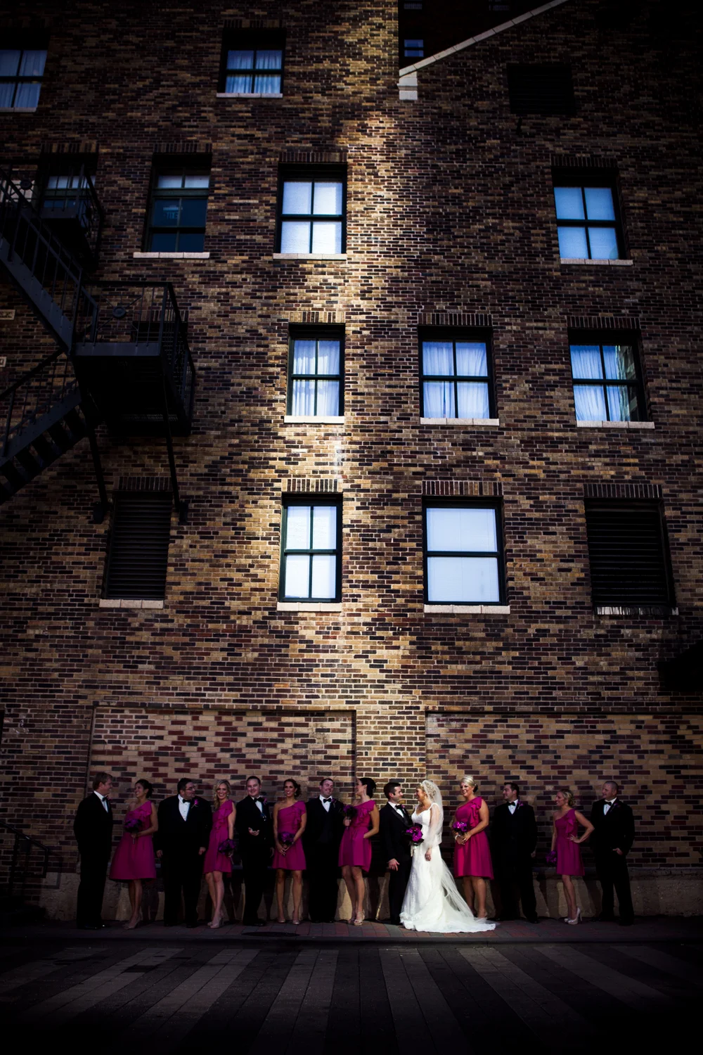 Liza & Nate - Kansas City, MO - We had scouted this location the day before and I really just loved this brick wall and staircase. When we jumped out of the bus, to my surprise (and excitment) the setting sun was sending a beam of light through the buildings behind me lighting up just a strip of the wall all the way to the ground. I stuck Liza and Nate in the light, just hoping, it would have the effect I saw in my head.