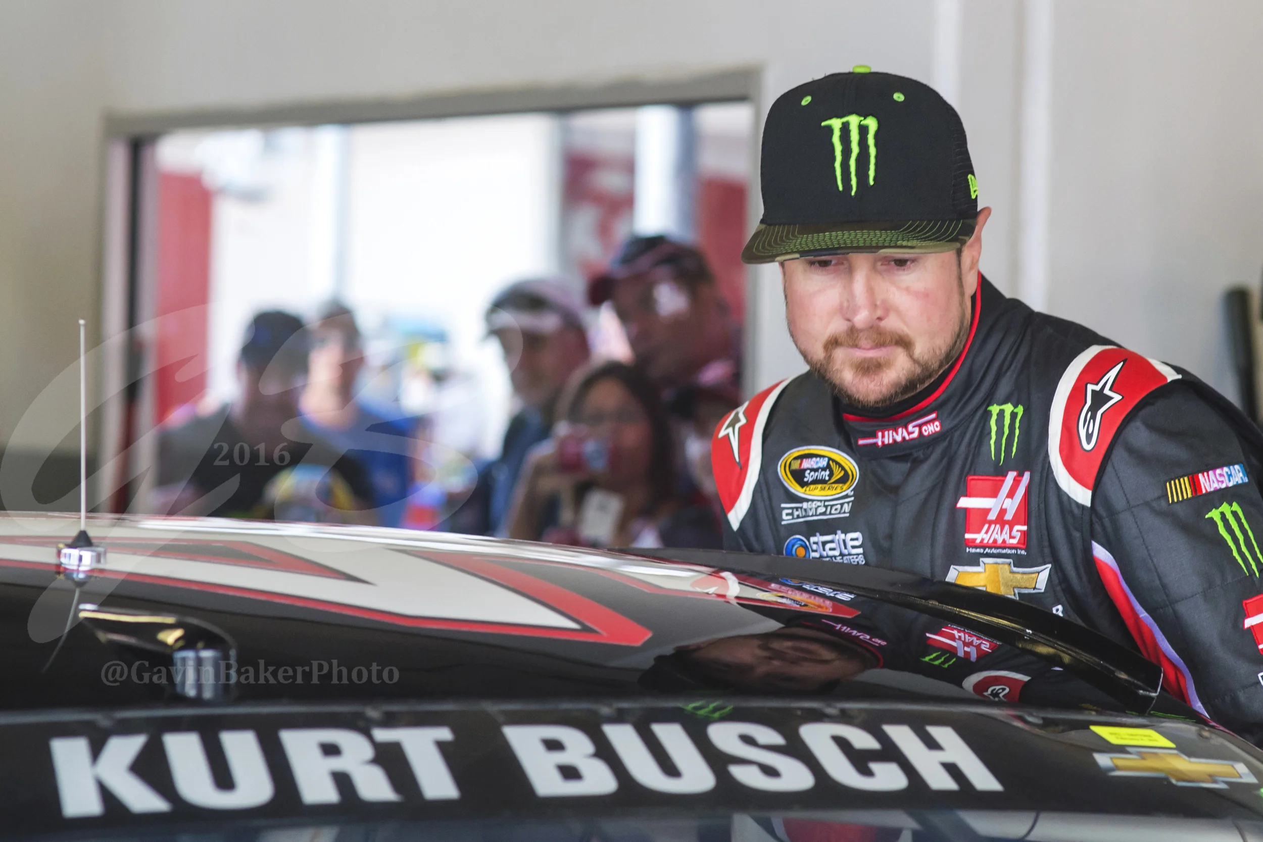 Fans look on and snap pictures from behind the viewing area of the garage as Kurt Busch climbs into his racecar