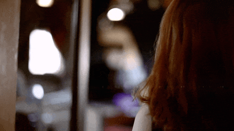 Close-up of a woman with long red hair looking away indoors with blurred background.