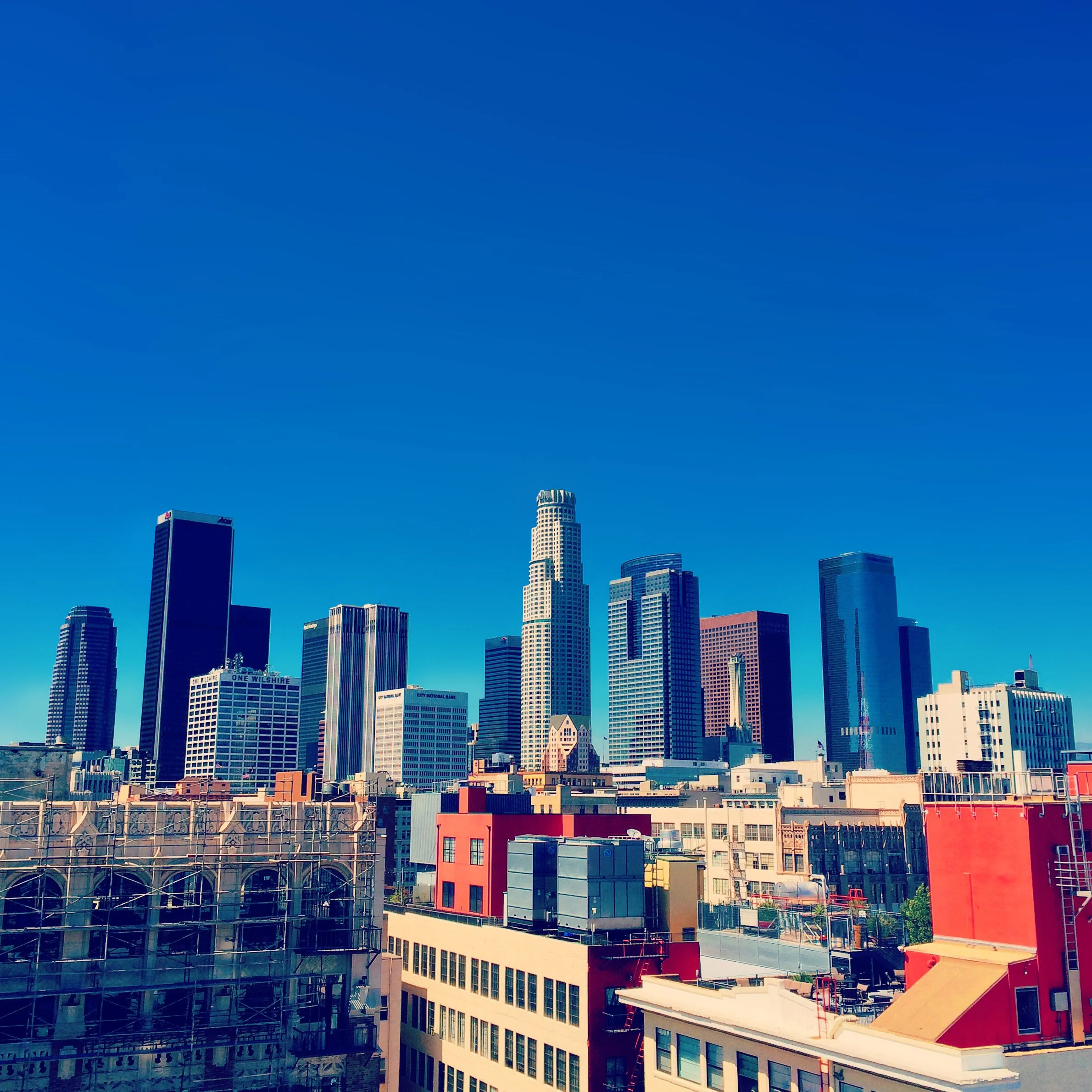 Los Angeles city skyline with tall skyscrapers against a clear blue sky, with various colorful buildings in the foreground.