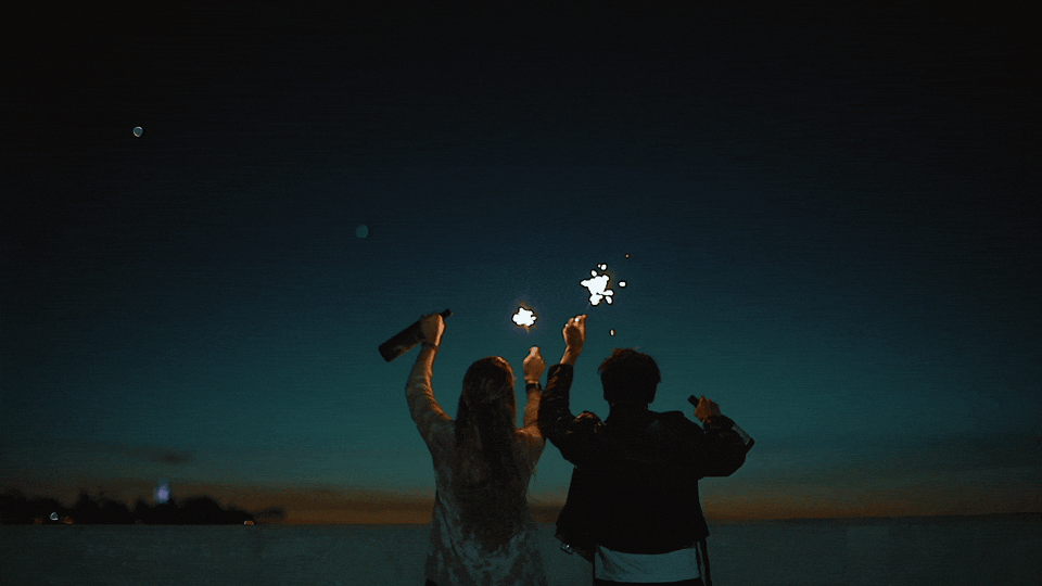 Two people celebrating on a beach at dusk with sparklers.