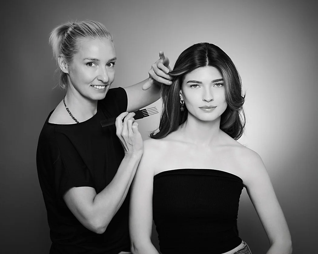 A hairstylist styling a woman's hair in a professional photo shoot setting, black and white photo.