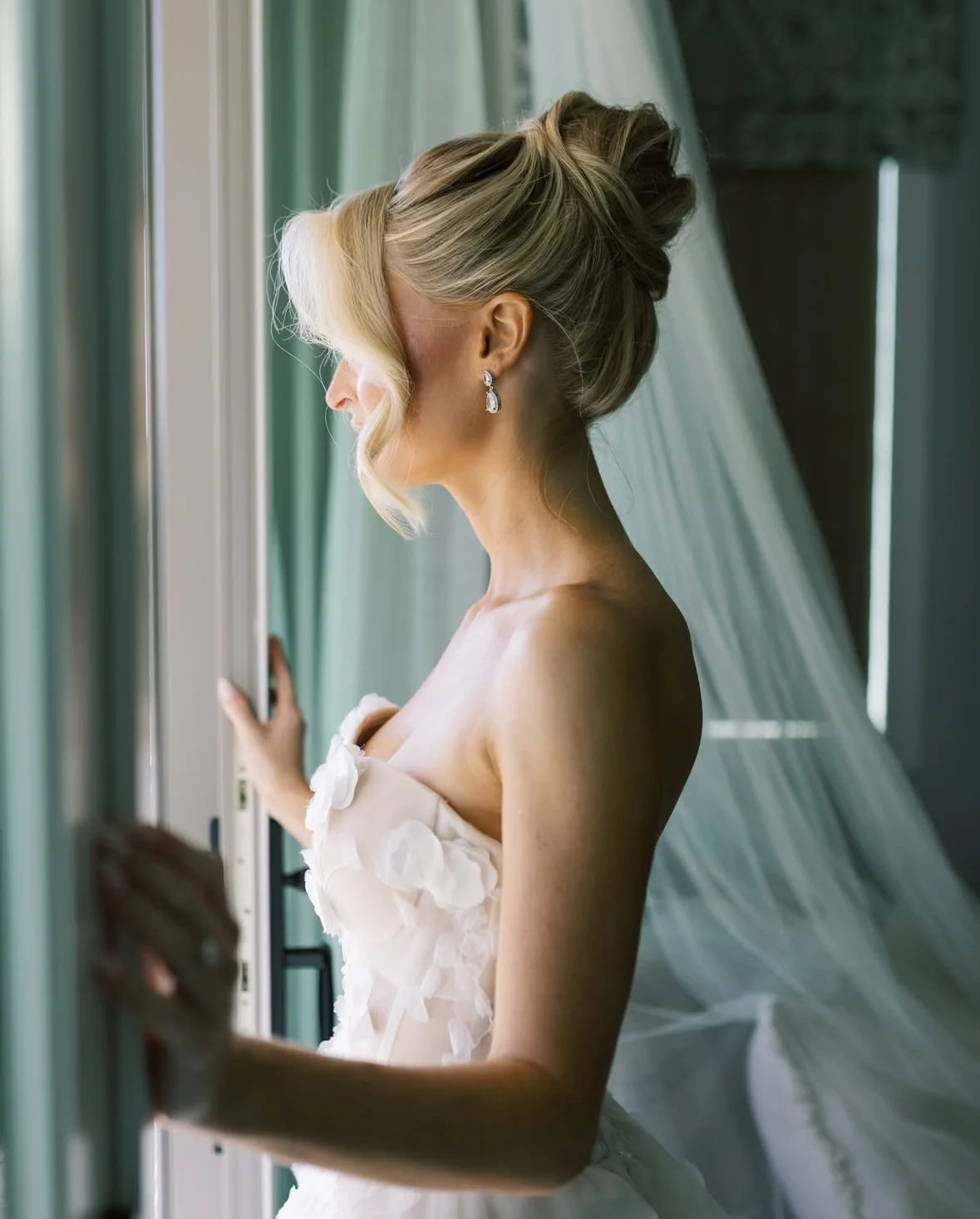 Bride looking out a window with an elegant updo hairstyle.