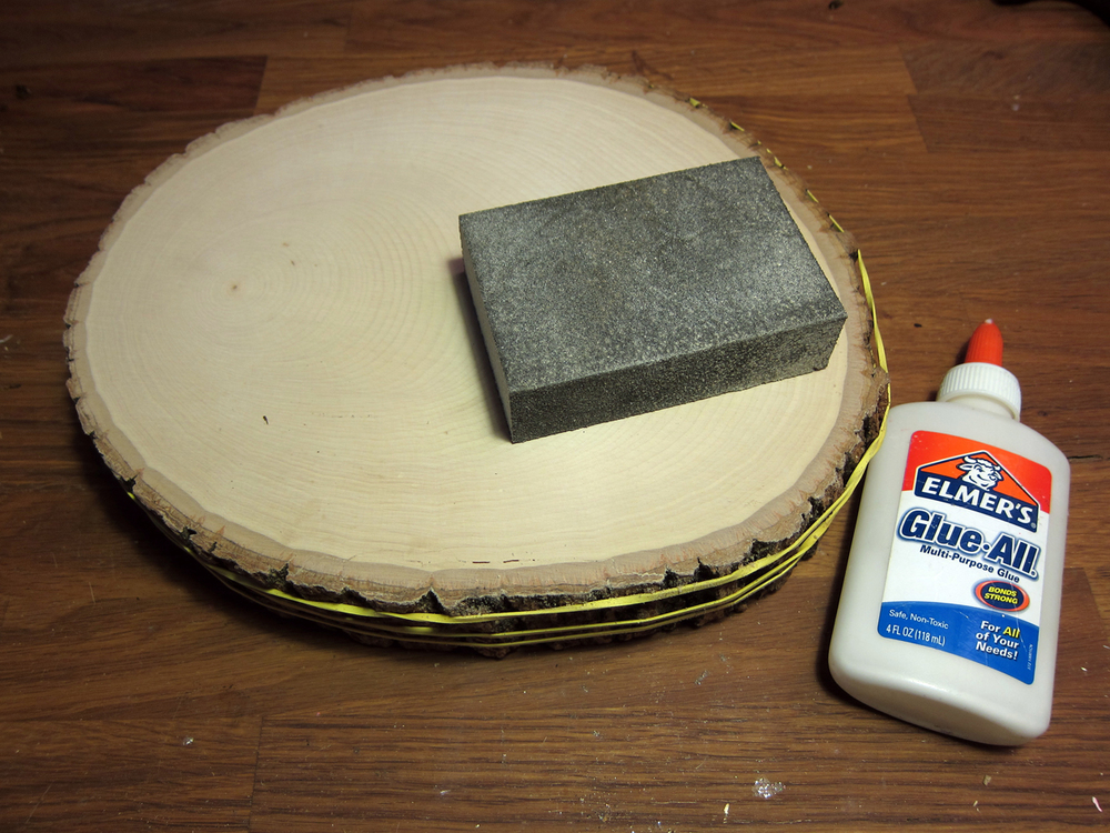  Clean surfaces by removing all dust and wood shavings. Use a wood glue to affix the bark edge back to the basswood round. Rubber-bands will help hold the piece in place as it dries.&nbsp;Sand front of basswood round with a fine grit sand paper.   