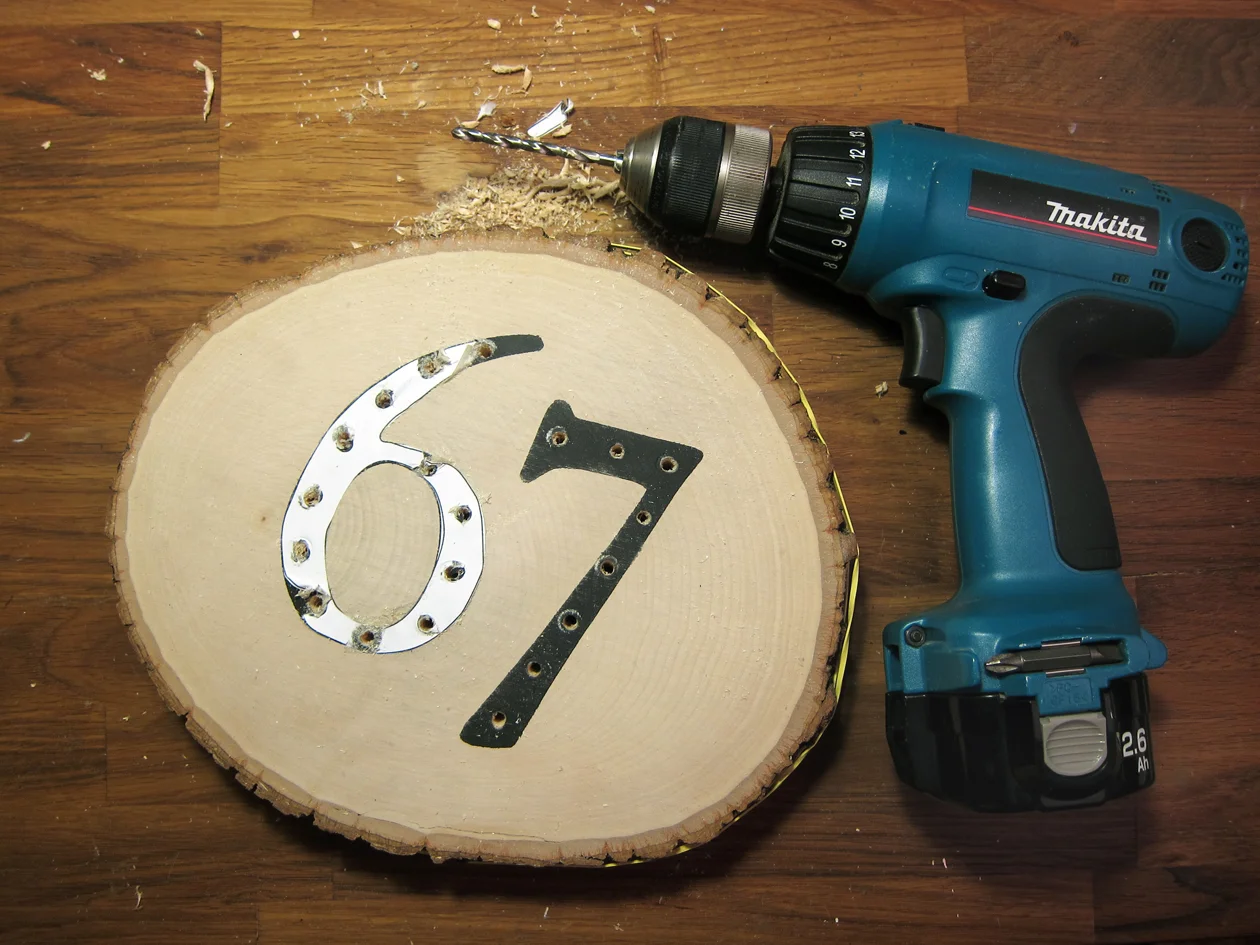 With the numbers that were cut from stencil, evenly mark 20 light holes. Tape paper numbers over painted numbers on basswood. With a drill affixed with an 11/64" bit, drill through basswood round on marks.
