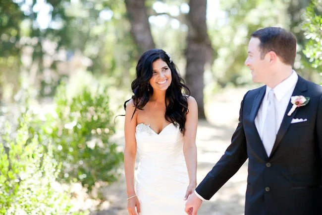 A bride and groom holding hands outdoors, smiling at each other during their wedding.