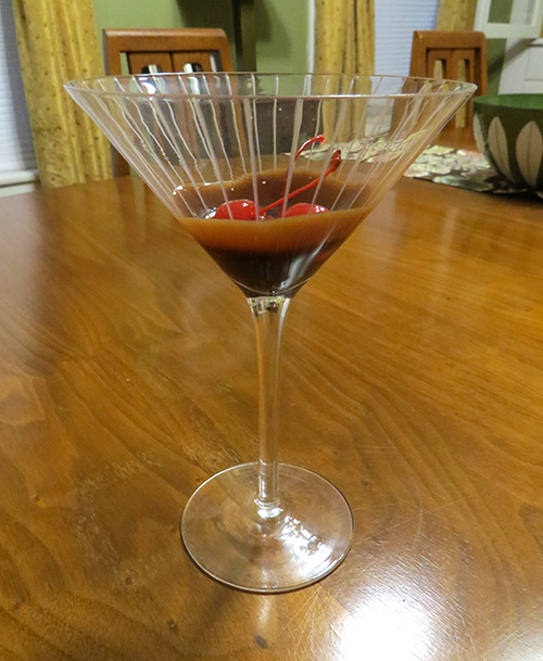 Prepping the drink with chocolate syrup and cherries at the bottom of the glass.