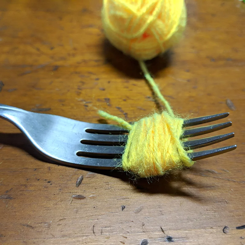 Making mini pompoms with a fork and some yarn
