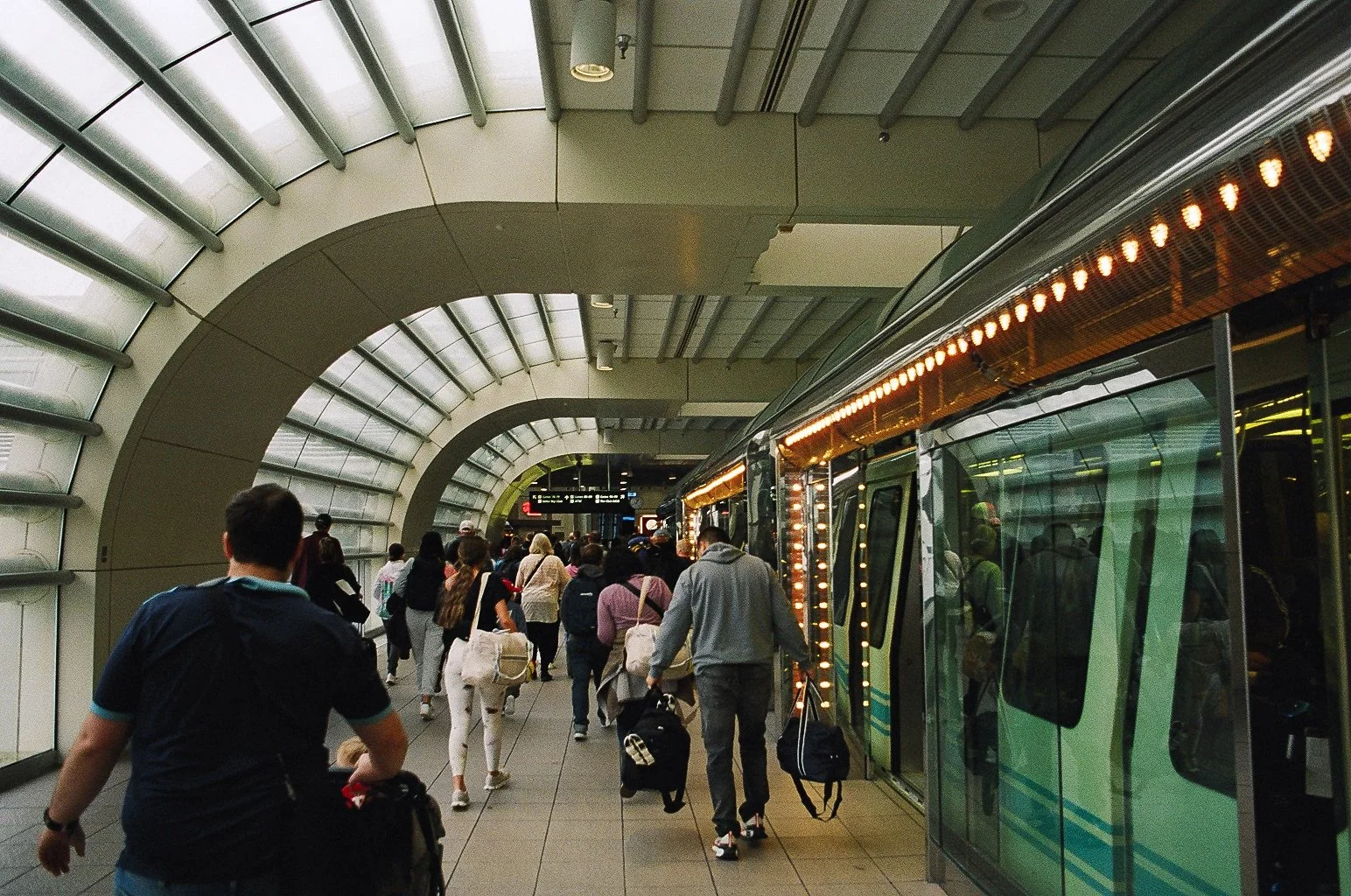 People boarding a modern, illuminated train at an underground station with curved, glass-paneled architecture.