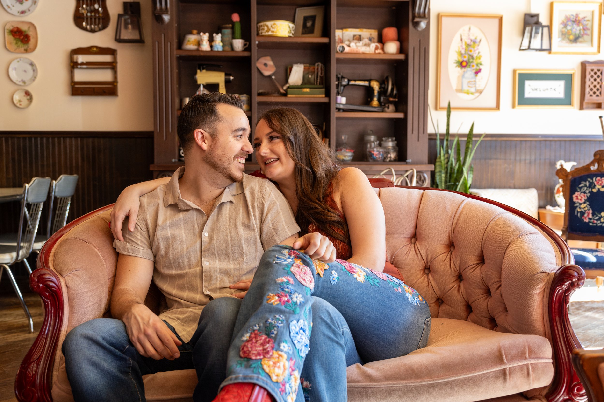 A young couple is sitting on a vintage pink sofa in a cozy living room, sharing a happy moment and smiling at each other.