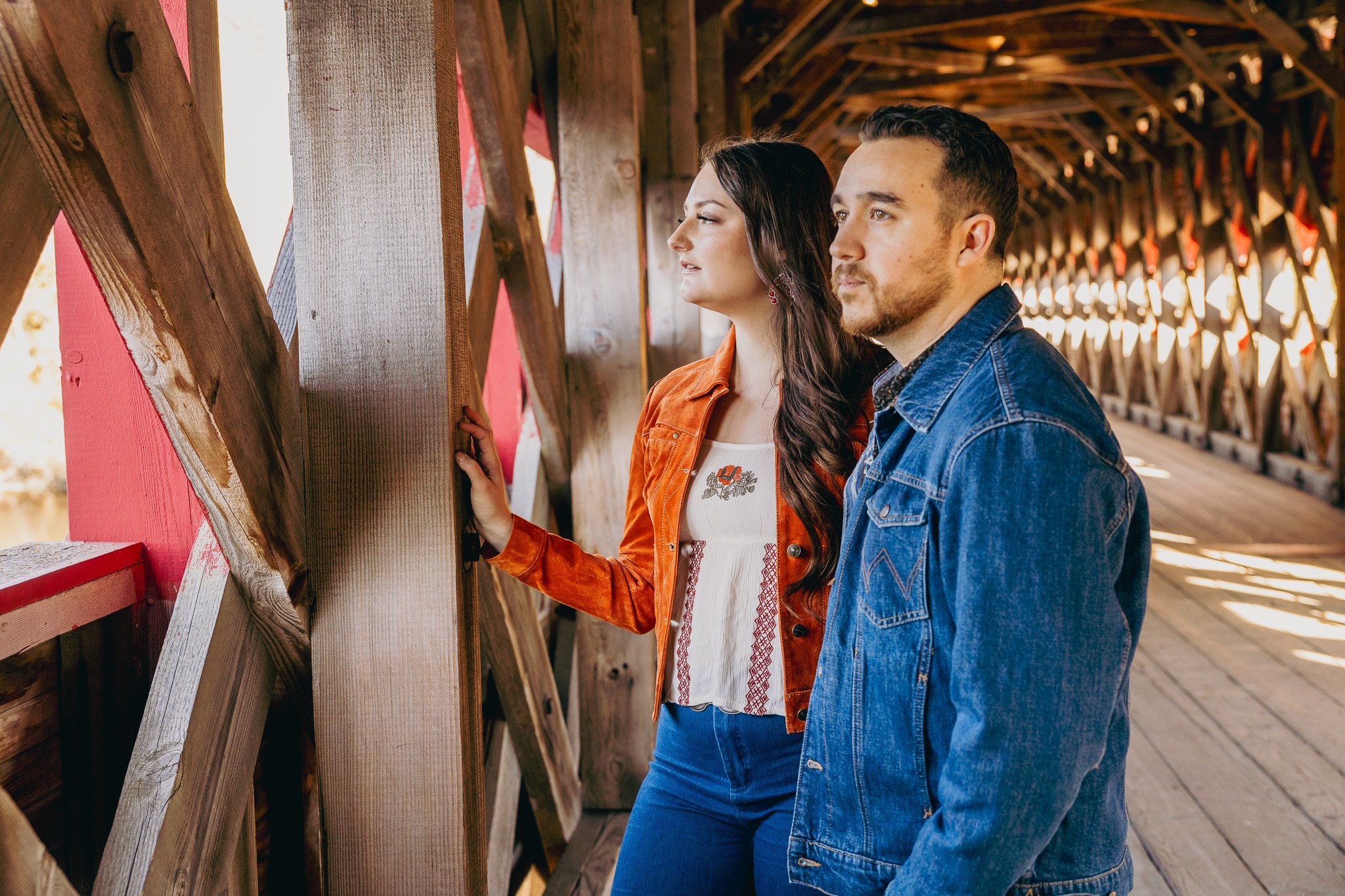 A man and woman standing in a wooden covered bridge, looking out at the scenery.