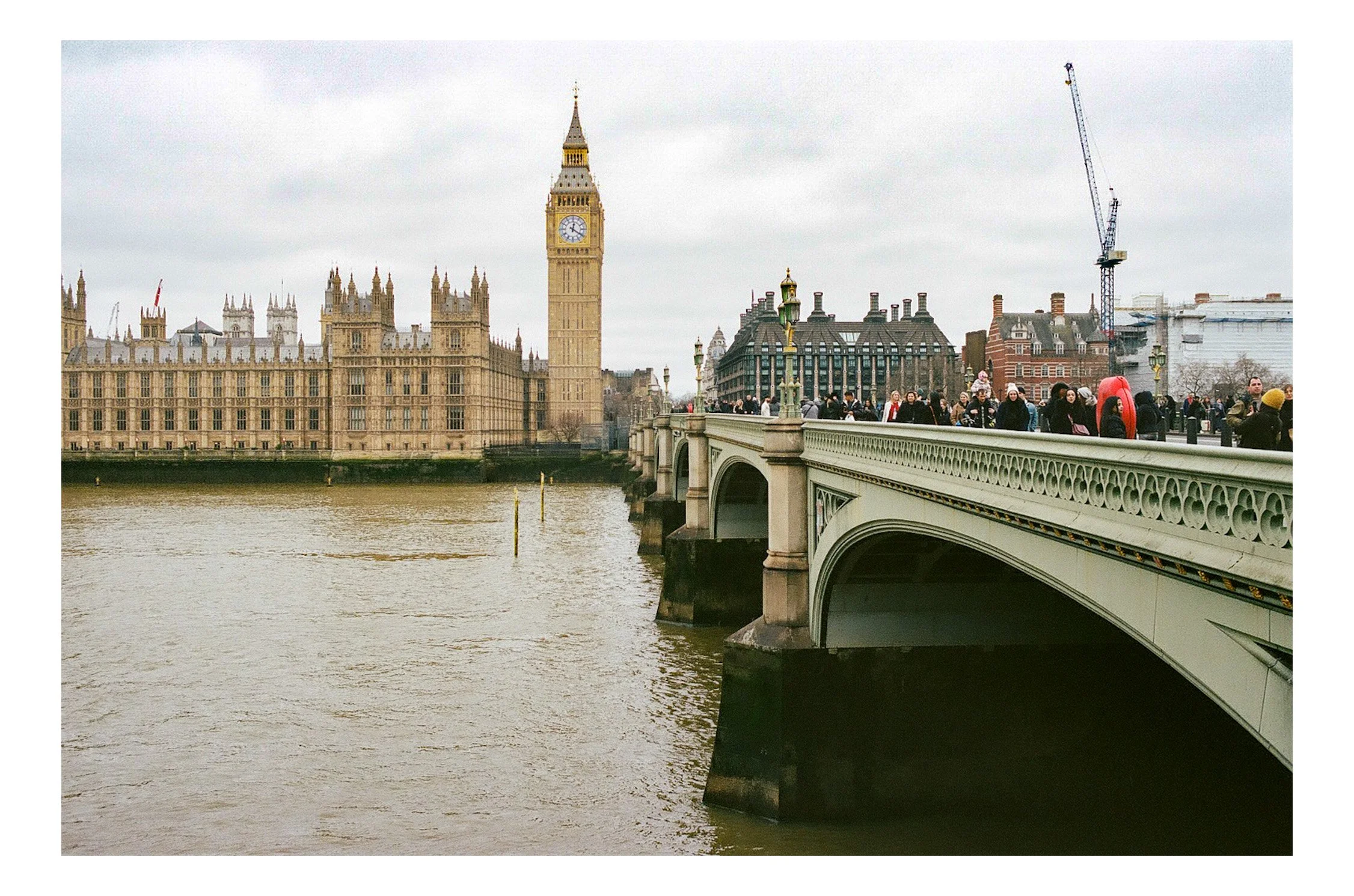 View of Westminster Bridge with Big Ben and the Palace of Westminster in the background, over the River Thames, with pedestrians walking on the bridge on a cloudy day.
