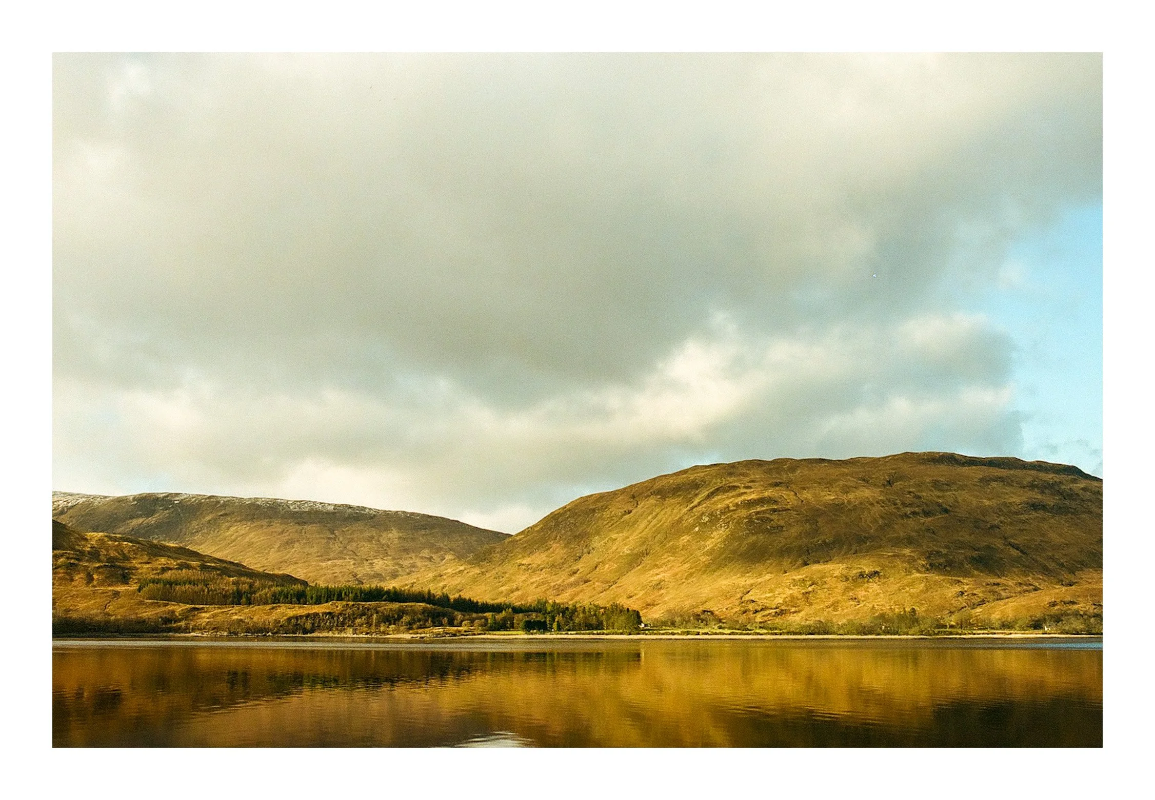 Scenic view of misty mountains reflecting on a calm lake under cloudy sky.
