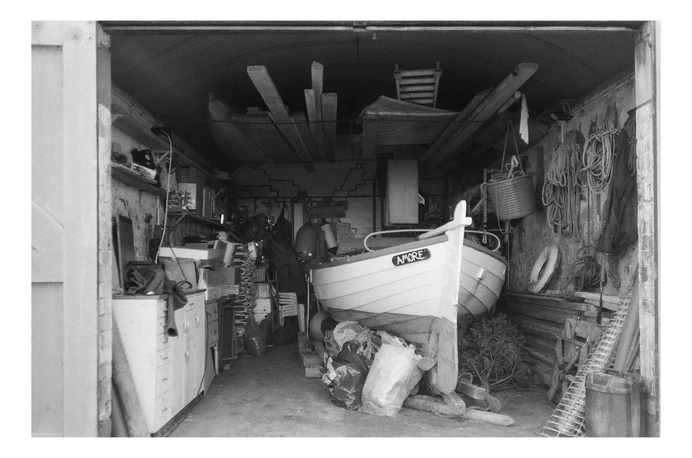 A cluttered garage with two boats, various tools, hoses, and supplies stored on shelves and hanging on the walls.