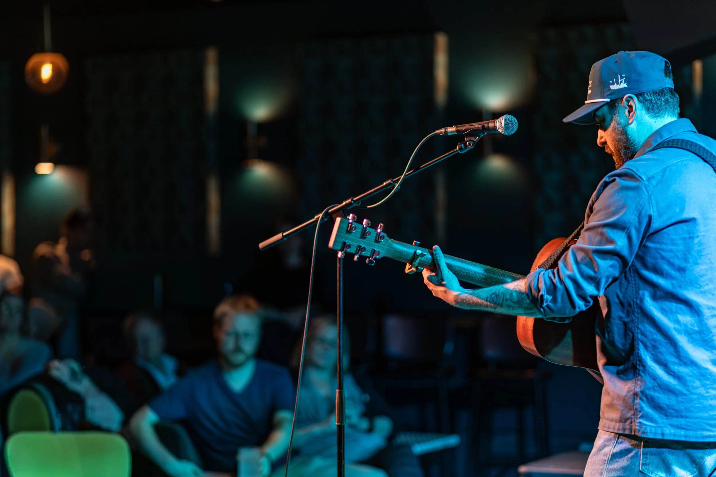 Musician performing on stage with guitar in front of audience in a dark venue