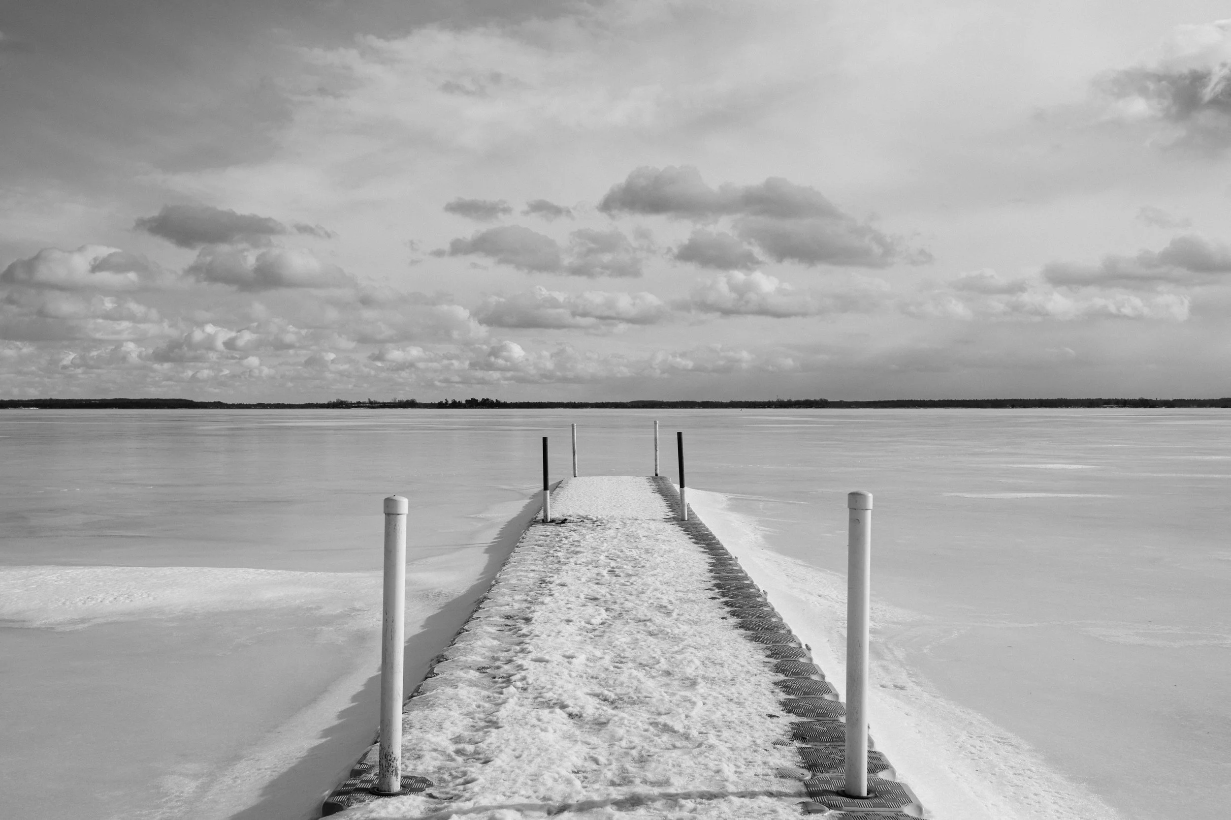 A snow-covered dock extending over a frozen body of water with a cloudy sky.