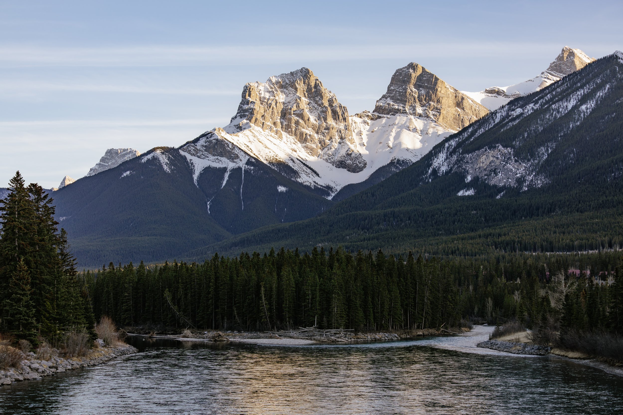 Snow-capped mountains over dense pine forest and a winding river in the foreground.