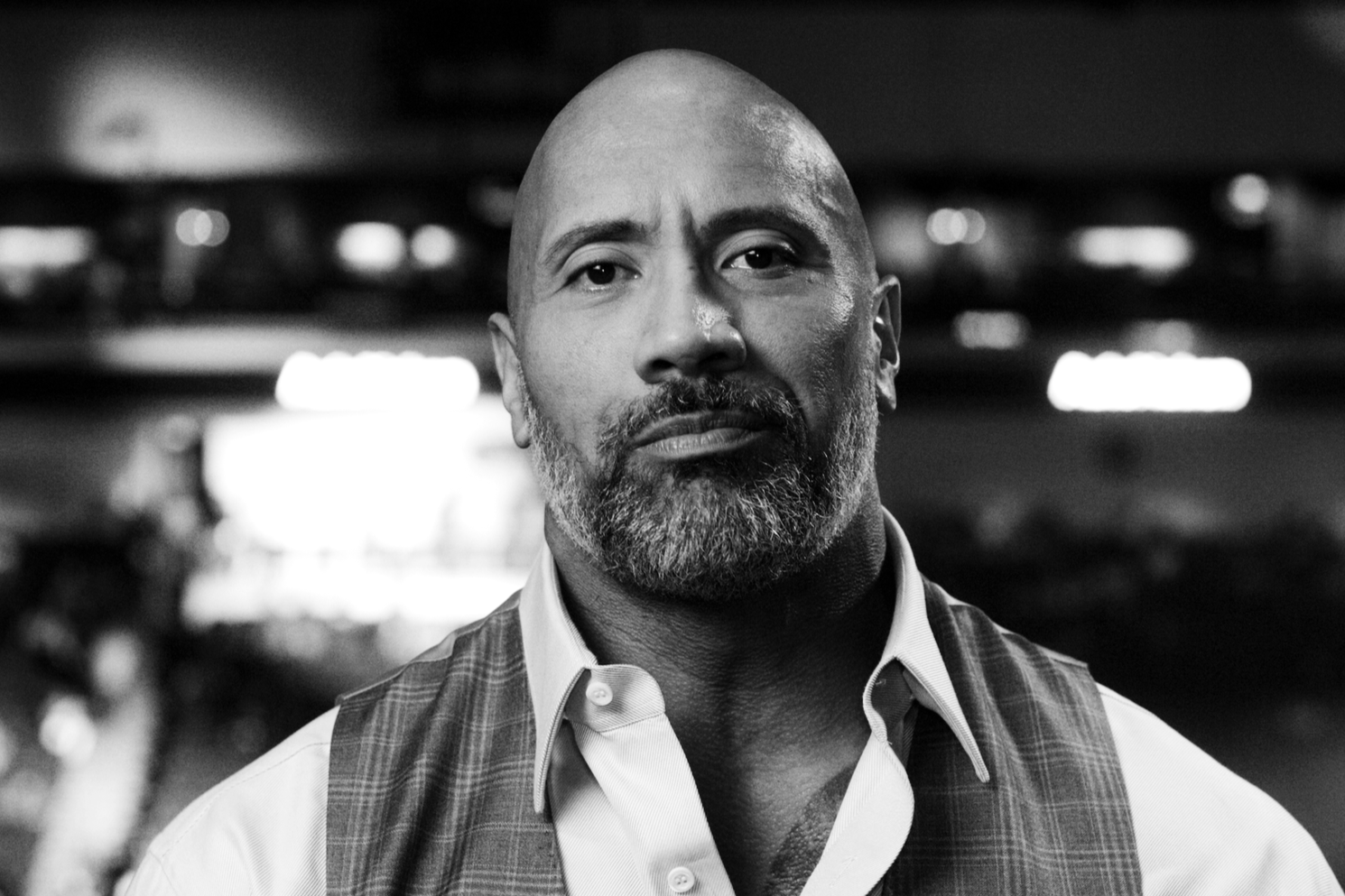 A muscular man wearing a hoodie and sleeveless shirt with a bull logo, standing in a gym with exercise equipment in the background.