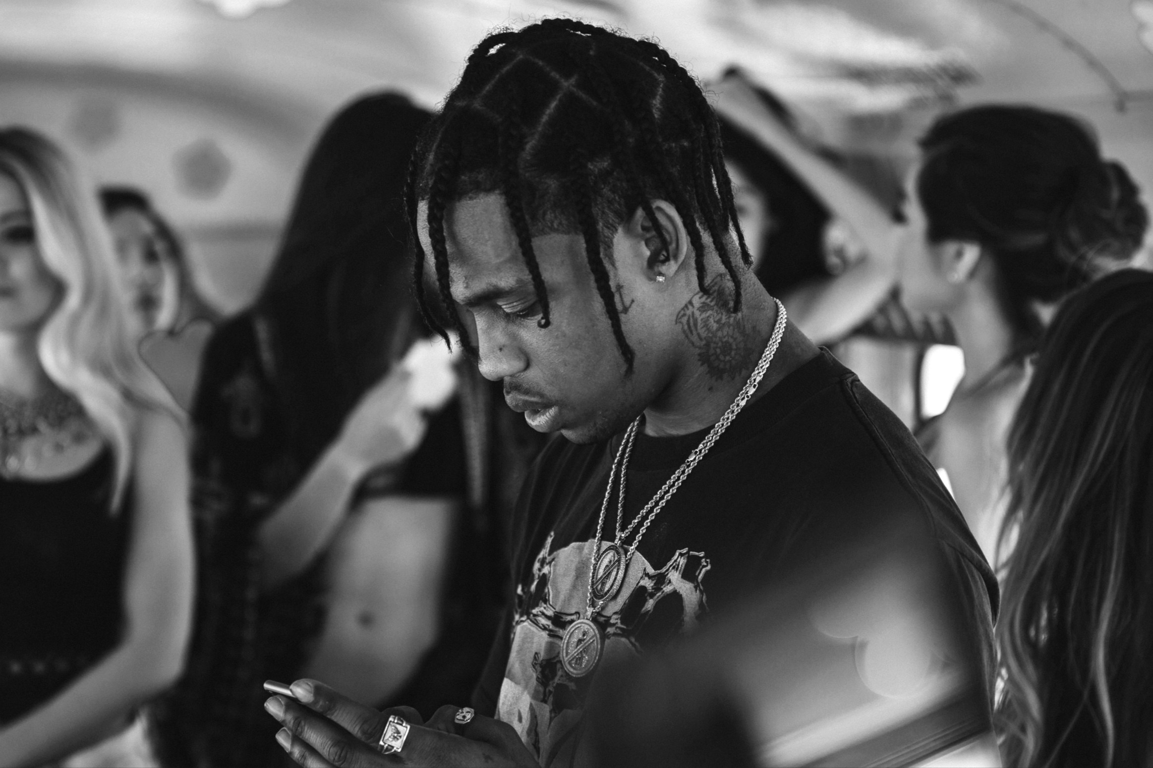 Black and white photo of a person with short, styled hair, wearing sunglasses, earrings, a chain necklace, and a shirt with a graphic design.