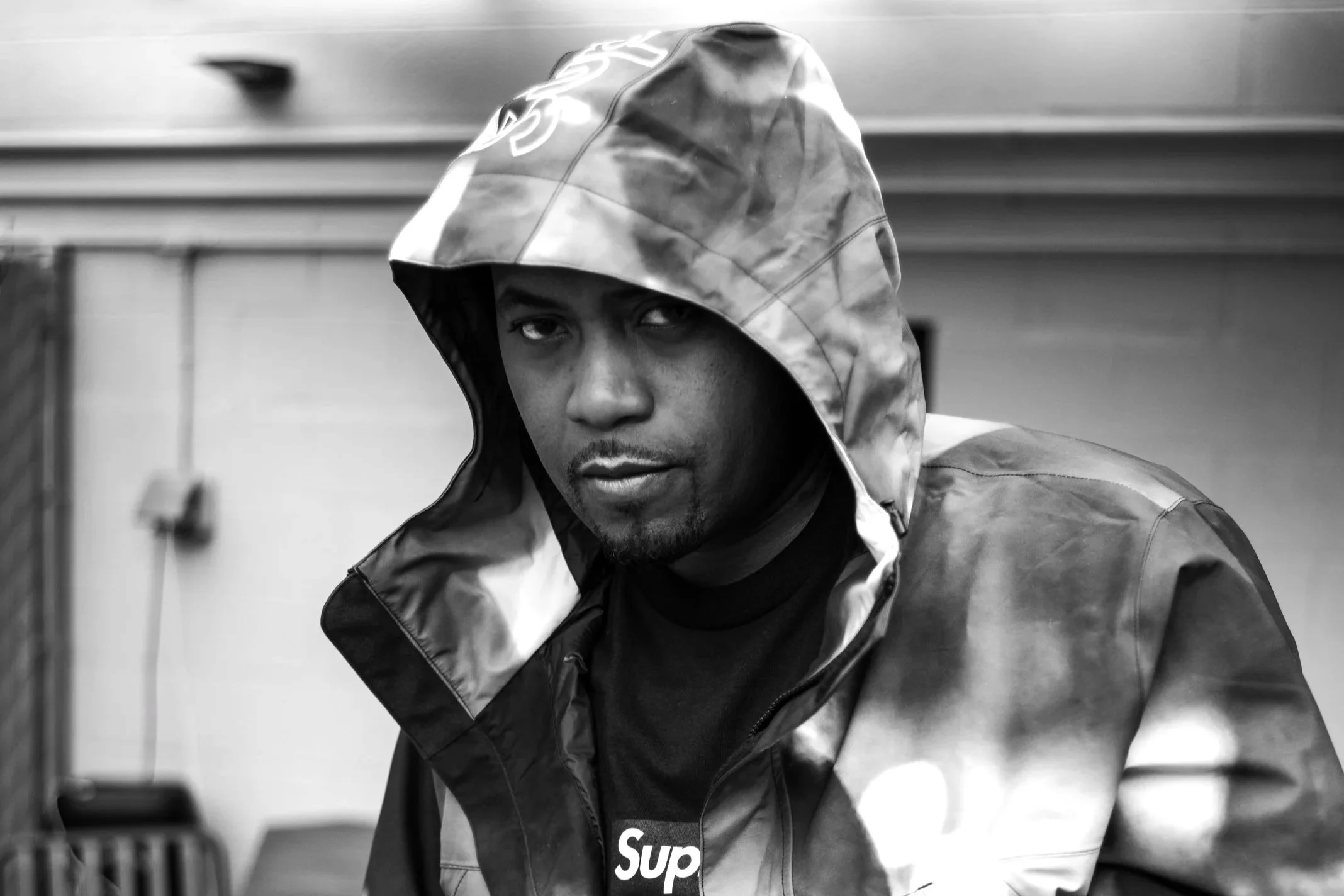 Black and white photo of a young man wearing a beanie and varsity jacket looking at the camera.