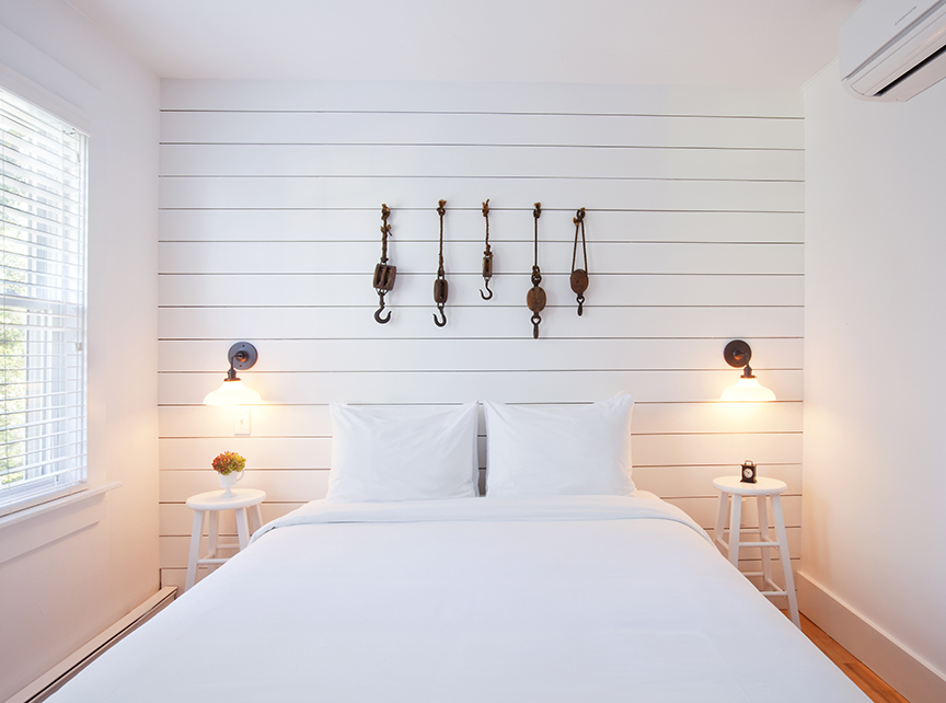 bedroom with white walls, white bed, wooden artwork