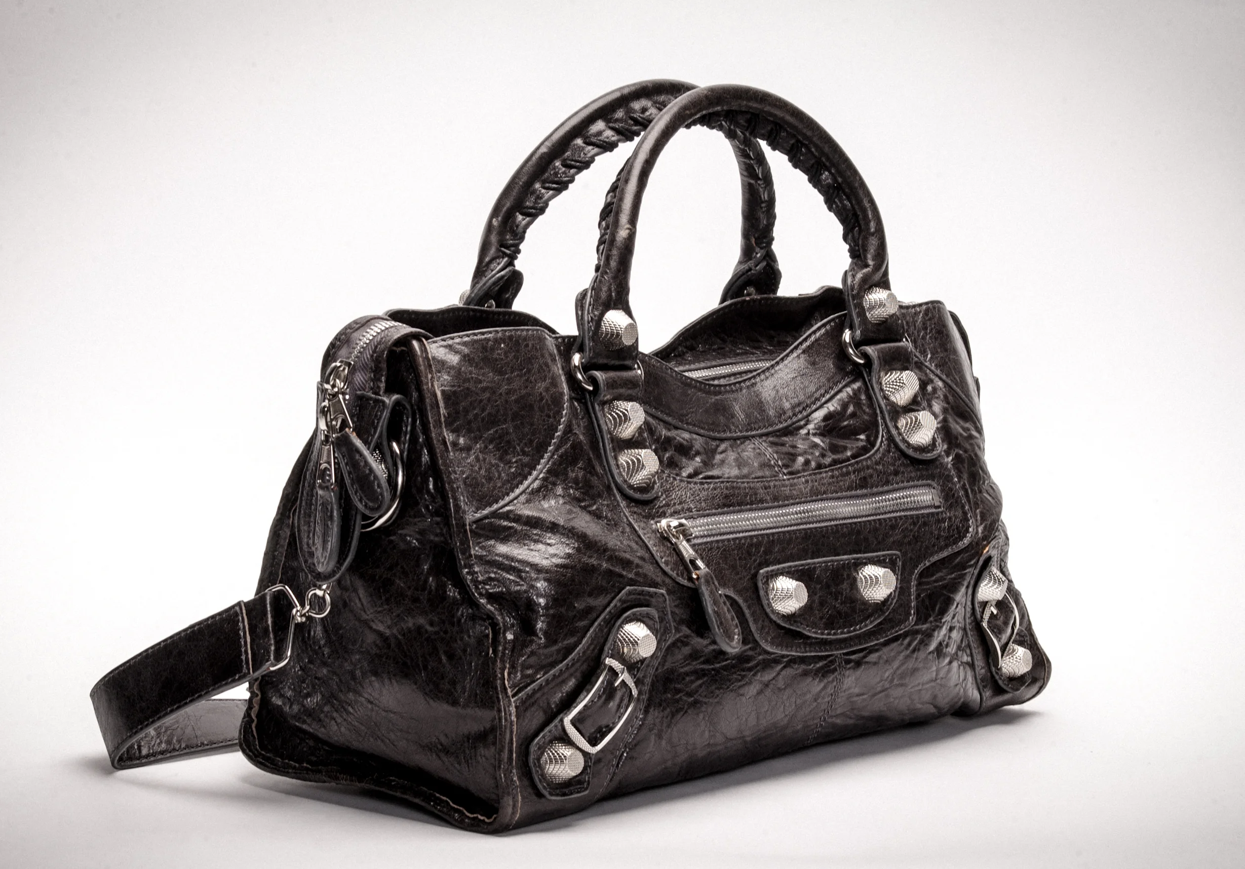 Luxury black leather handbag with metal accents and braided handles on a white background.