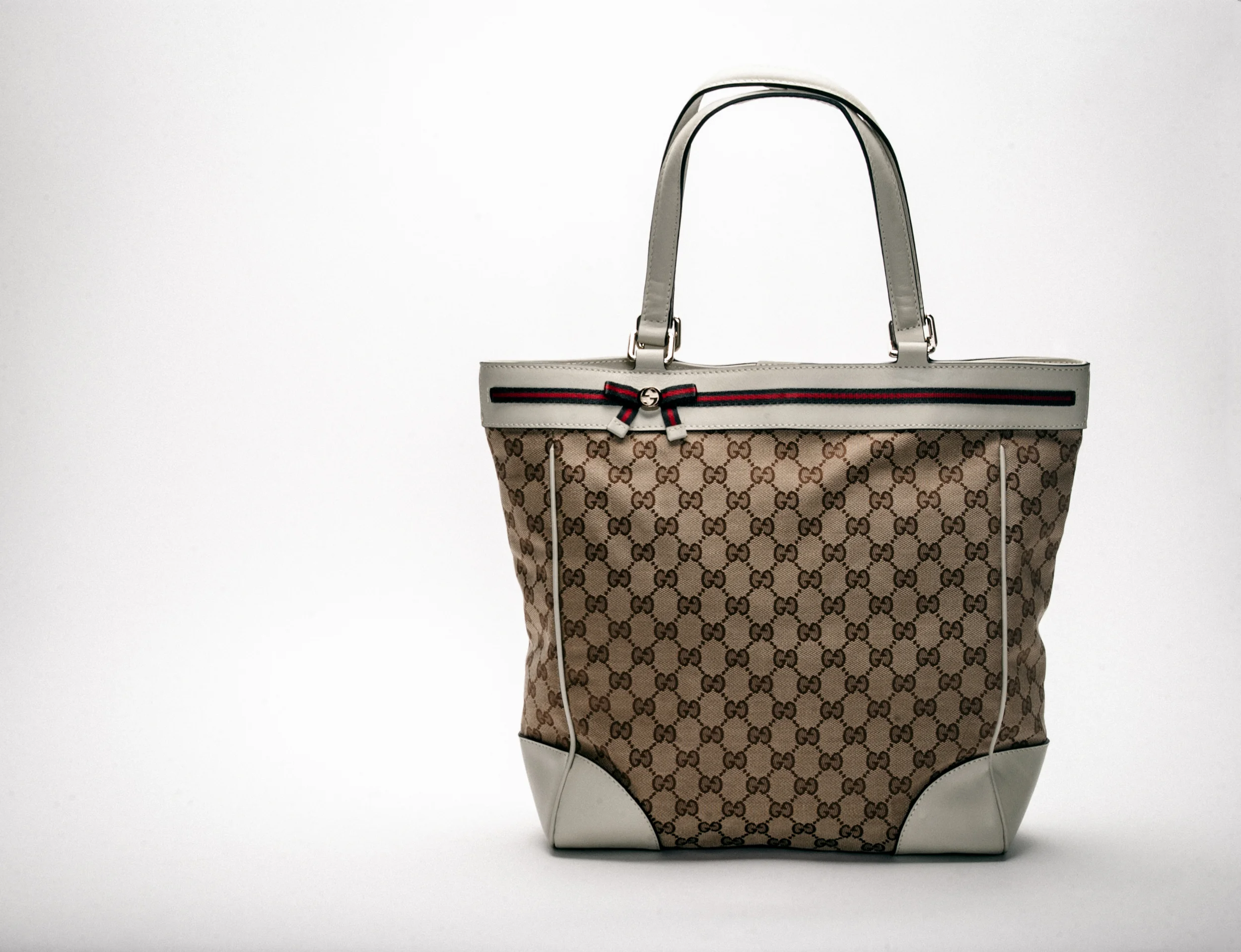 Stylish designer handbag with logo pattern and white handles on a plain background.