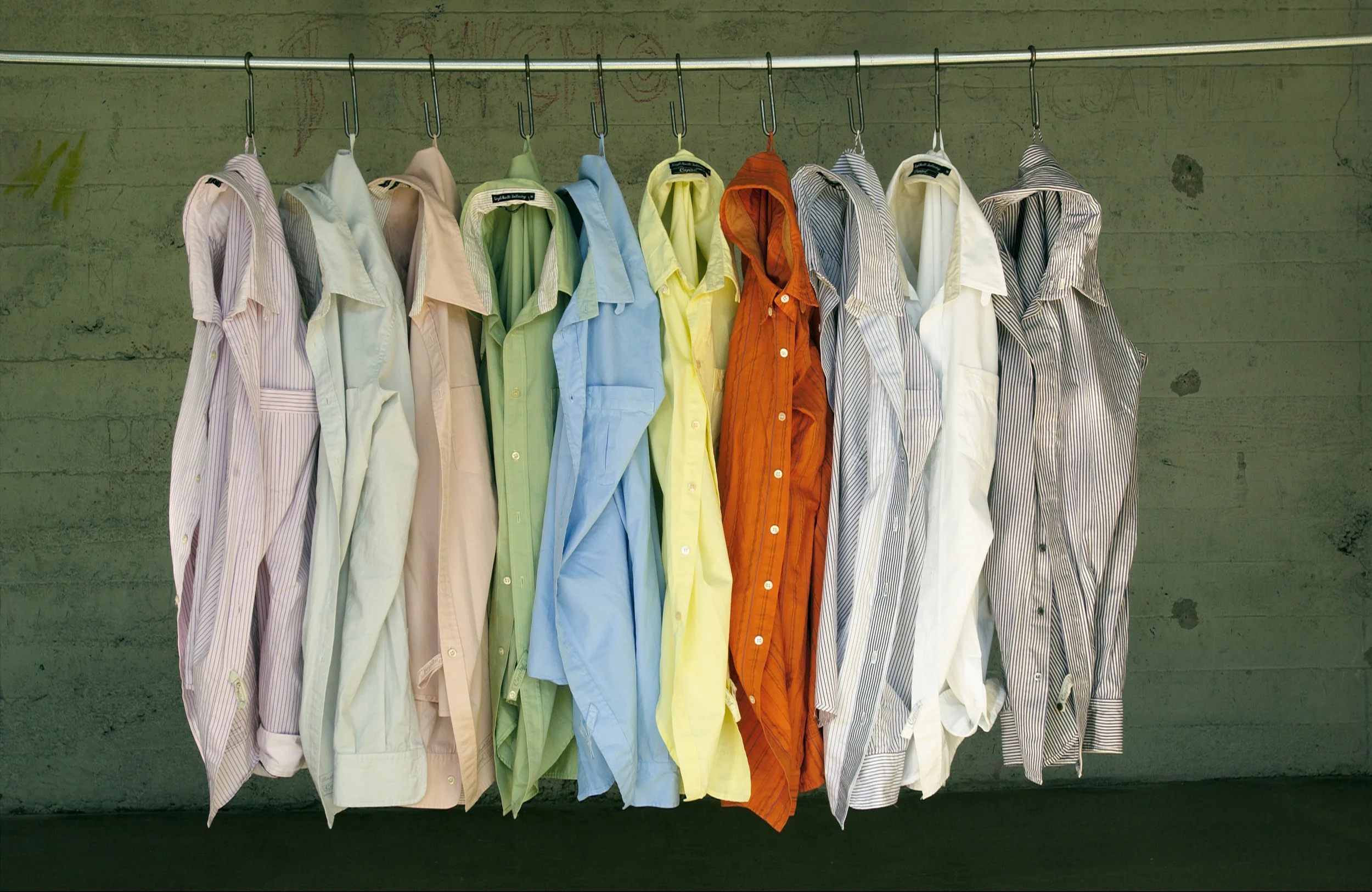 Row of colorful collared shirts hanging on hangers against a concrete wall.