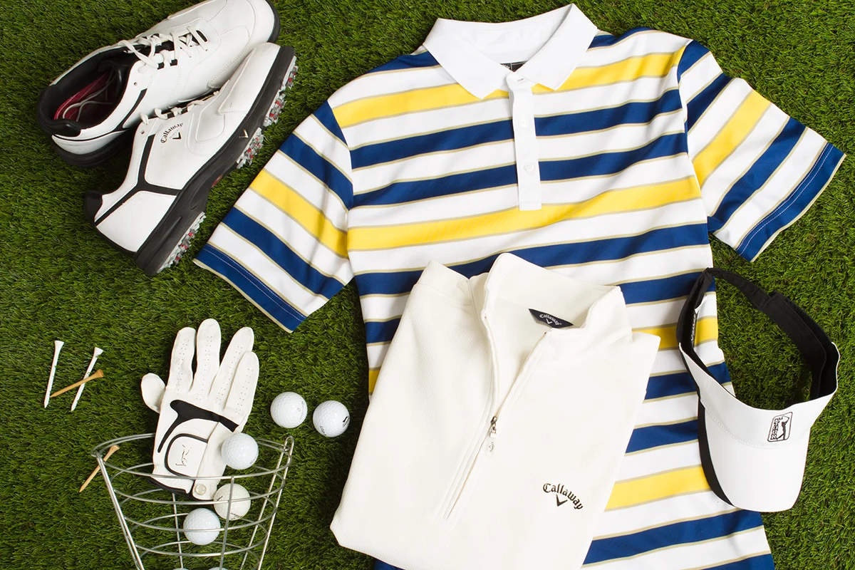 Golf apparel and accessories, including Callaway shoes, striped polo shirt, white golf pullover, visor, golf gloves, tees, and balls on grass.
