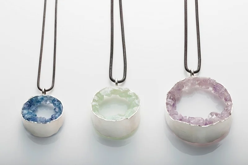 Three geode necklaces with crystal pendants in blue, green, and purple on metal chains