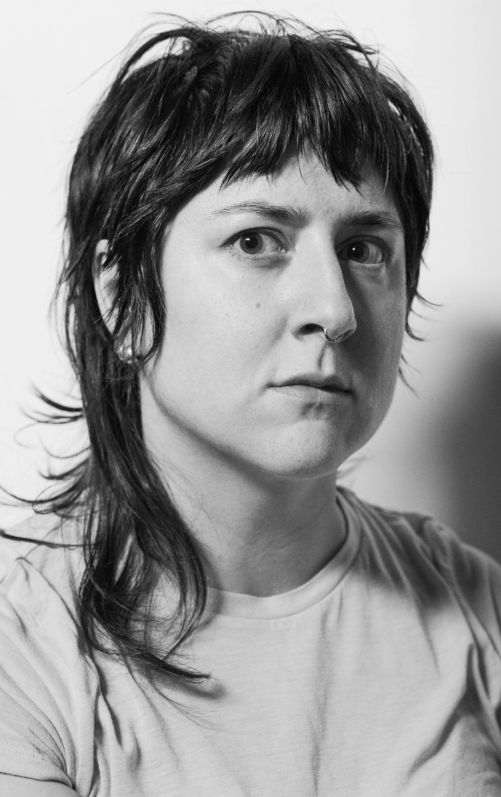 Black and white self-portrait of the artist. Annie is looking directly in the lens, her hair is a messy shag and she's wearing a white tshirt.