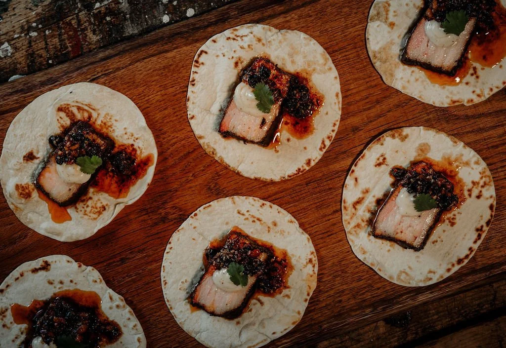 The perfect tacos on a wood table. Pork Belly from Applecroft catering.