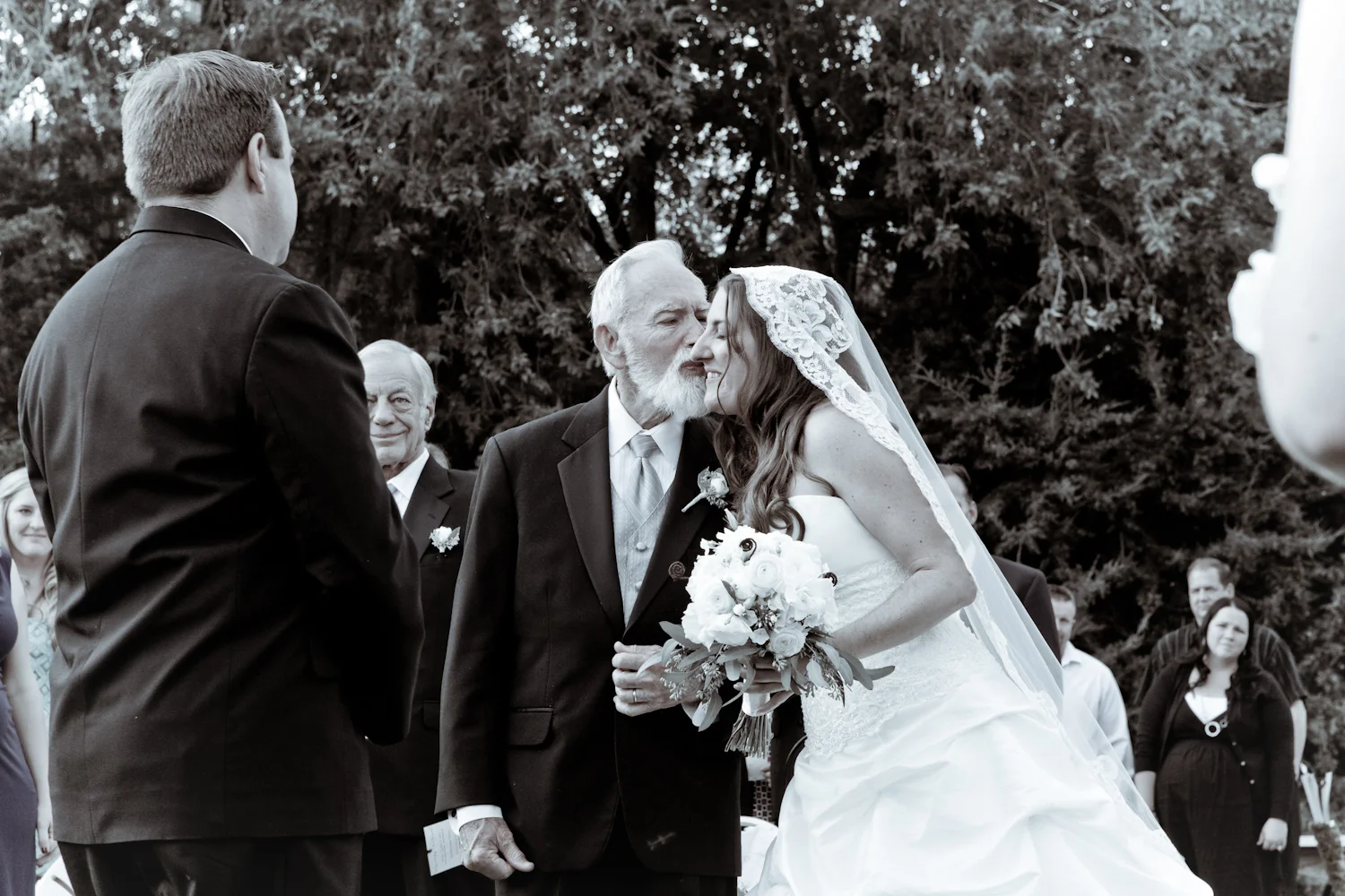 Loving father kisses his daughter on the cheek as he gives away the bride at outdoor wedding ceremony.