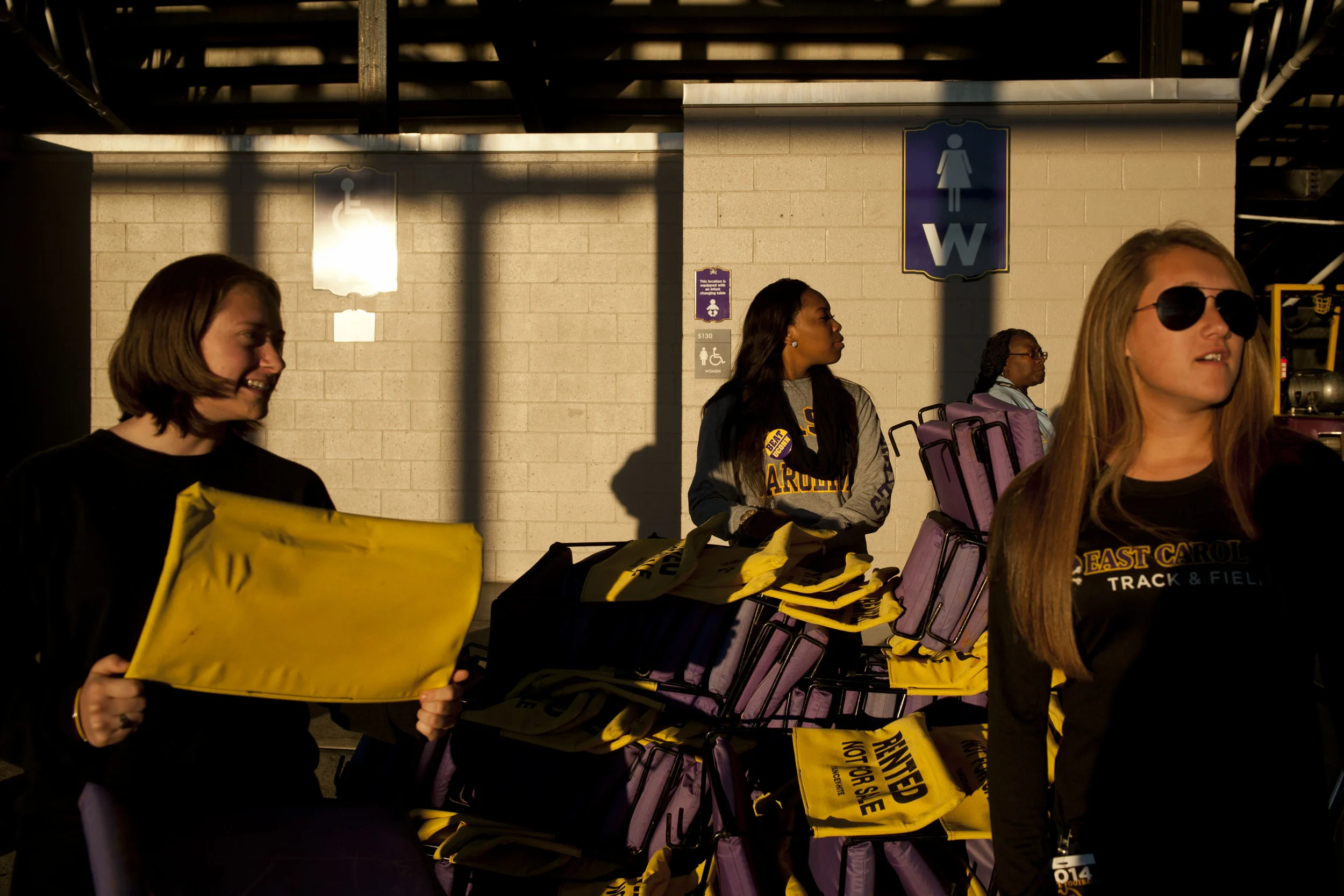 Jacquelyn Nance, left, sophomore, Taikasha Quattlebaum, freshman, and Emily Grimes, sophomore, rent seat backs to benefit the Air Force ROTC during the East Carolina game against Connecticut in Greenville, NC on Thursday, October 23, 2014. Photographed for The New York Times.