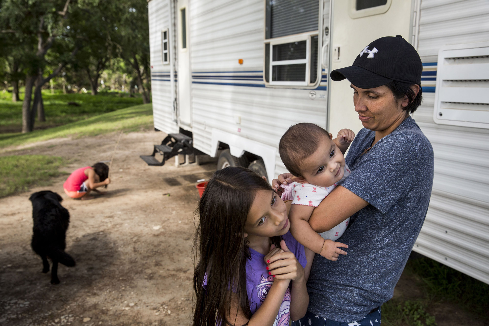 Cielo Bamberger, 10, and Esmebella Bamberger, 9 months, hang on their mother Glenda Bamberger while their sister Serenity Bamberger, 7, digs in the dirt outside of their RV on their property in Blanco, Texas on July 1, 2015. The family is living in the RV, which is parked in front of their flood-damaged home, while they build a new house on eight-foot pillars on the same property. The dog, known as Buddy or Bear, showed up on their property after the floods and has stayed since. Glenda said that she thinks he was carried far from his home in the floods, because none of their neighbors in the area have claimed him. 