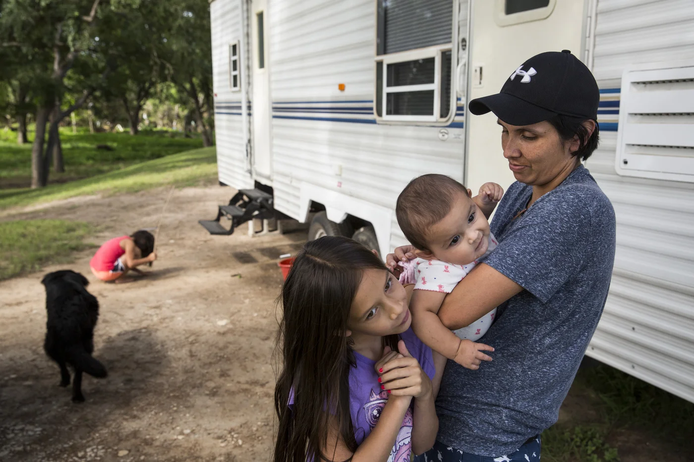  Cielo Bamberger, 10, and Esme Bella Bamberger, 9 months, hang on their mother Glenda Bamberger while their sister Serenity Bamberger, 7, digs in the dirt outside of their trailer on their property in Blanco, Texas, U.S. on July 1, 2015.  The family 