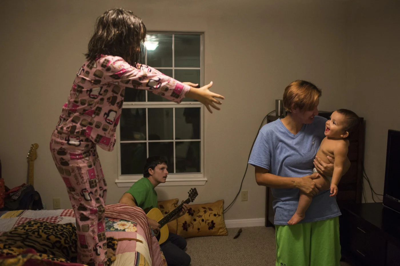  While Jarrell Bamberger plays guitar, Serenity Bamberger stands on her parents' bed and reaches out towards her sister Esme Bella Bamberger, who is in Glenda Bamberger's arms, on their first official day living in their new home in Blanco, Texas on 