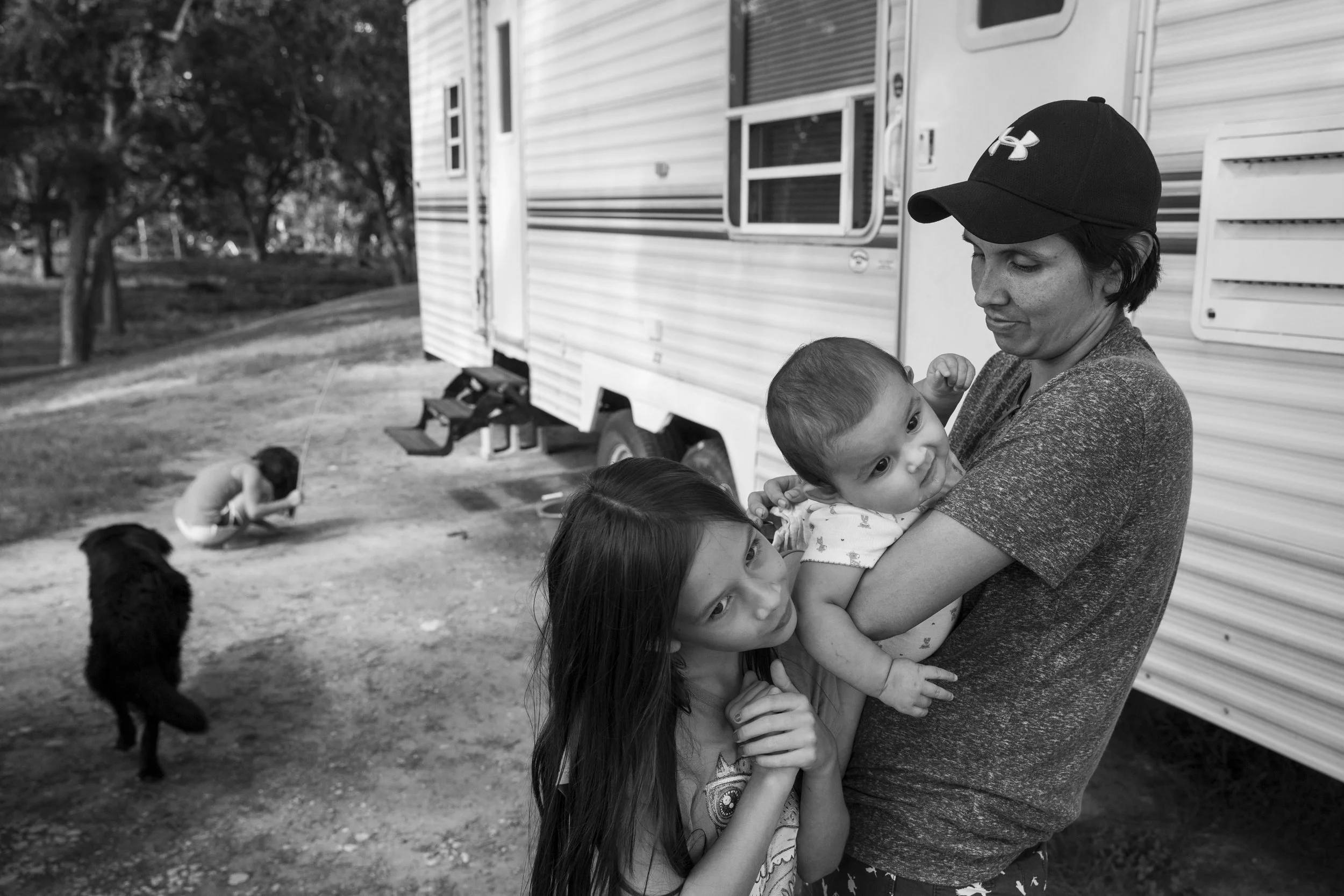  Cielo Bamberger, 10, and Esme Bella Bamberger, 9 months, hang on their mother Glenda Bamberger while their sister Serenity Bamberger, 7, digs in the dirt outside of their trailer on their property in Blanco, Texas, U.S. on July 1, 2015.  The family 