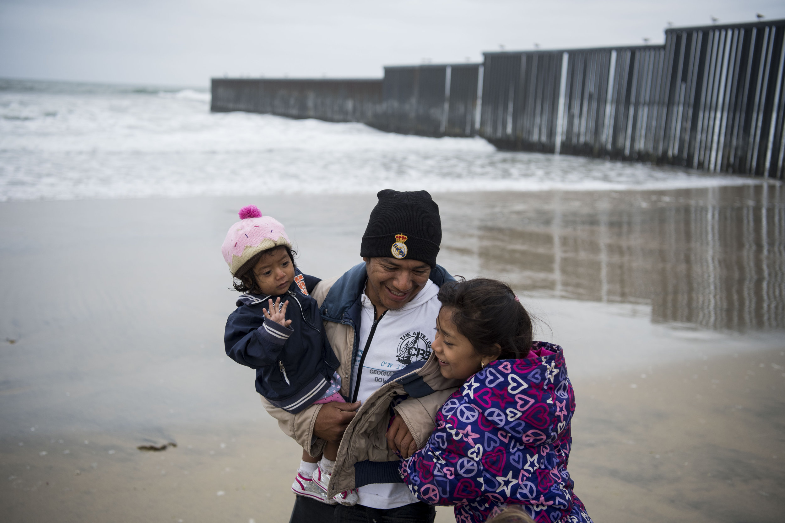 William Rafael Carranza Martinez laughs after running away from the waves with Jessica Carolina Dominguez Martinez, 1, and Elda Hidalia Martinez, 9, near the border wall before marrying his partner at the beginning of the March Without Borders at Friendship Park on April 29, 2018 in Tijuana, Mexico. Hundreds of migrants from Central America traveled for about a month across Mexico to reach the United States border. In the afternoon, the group, including the Martinez family, plans to go to the San Ysidro border crossing south of San Diego, California, where many of the migrants will seek asylum.