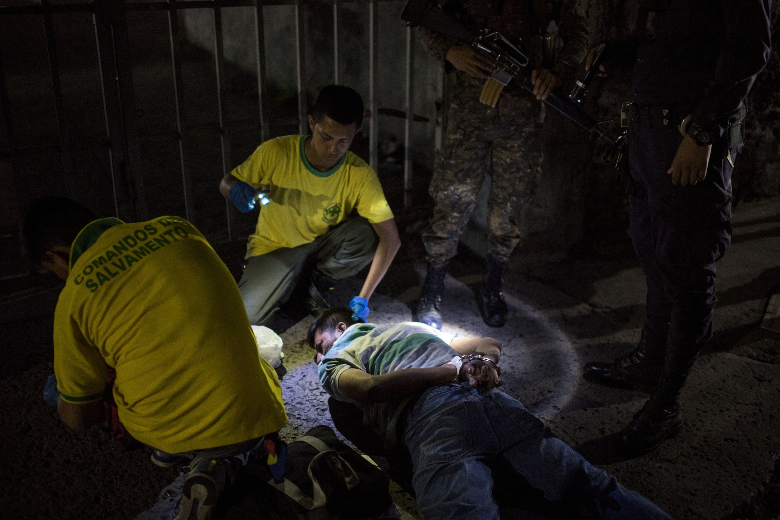 Police officers stand guard at the scene of a shooting while the Comandos de Salvamento attend to the shooter, who was also shot, on a street in San Salvador, El Salvador on September 29, 2018. Earlier that day there had been another shooting in the same area. The Comandos de Salvamento are a first responder volunteer group that aids in stabilizing and transporting people who have been victims of violence, accidents or need emergency medical care. Many volunteers became members of the group as a way to stay out of gangs.