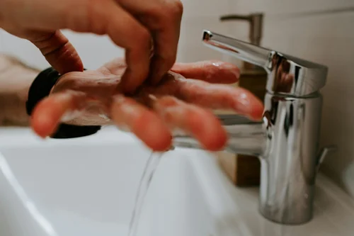Hands being washed with soap at a sink.
